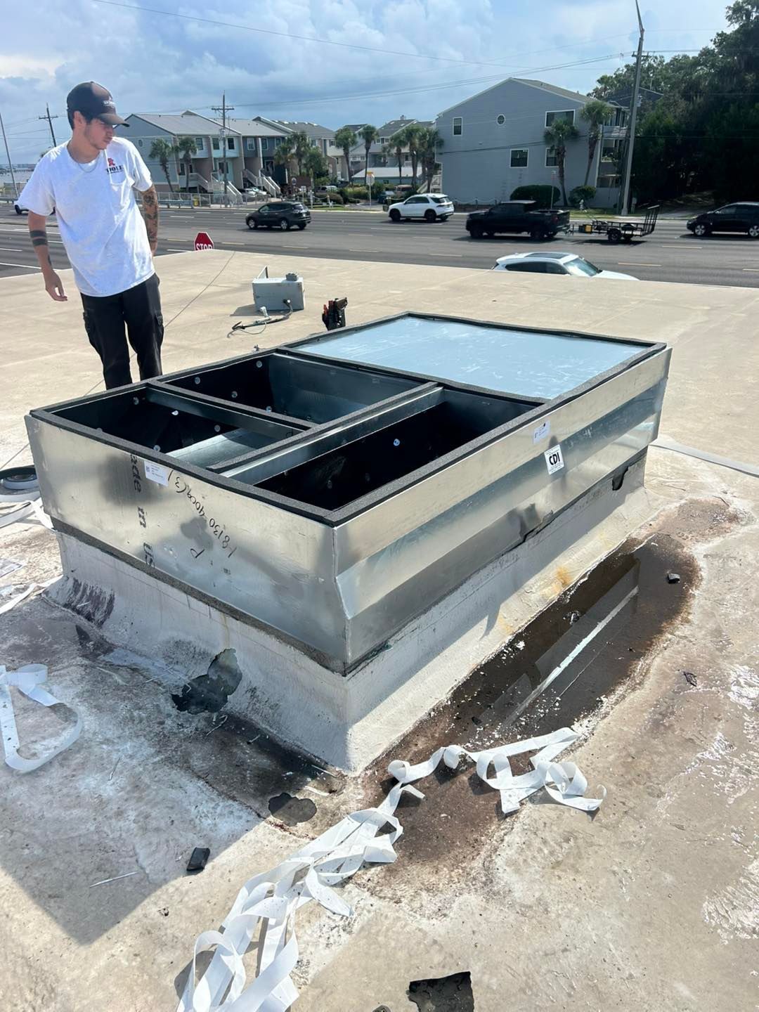 Man on roof near HVAC unit, possibly repairing, under a blue sky.