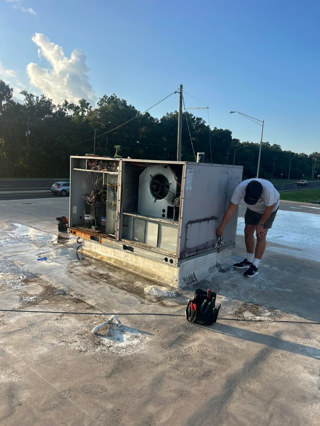 Person examining a rooftop air conditioning unit. Unit is exposed; a tool bag sits nearby.