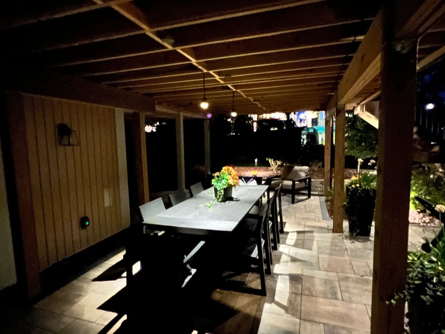 A patio with a table and chairs under a pergola at night.