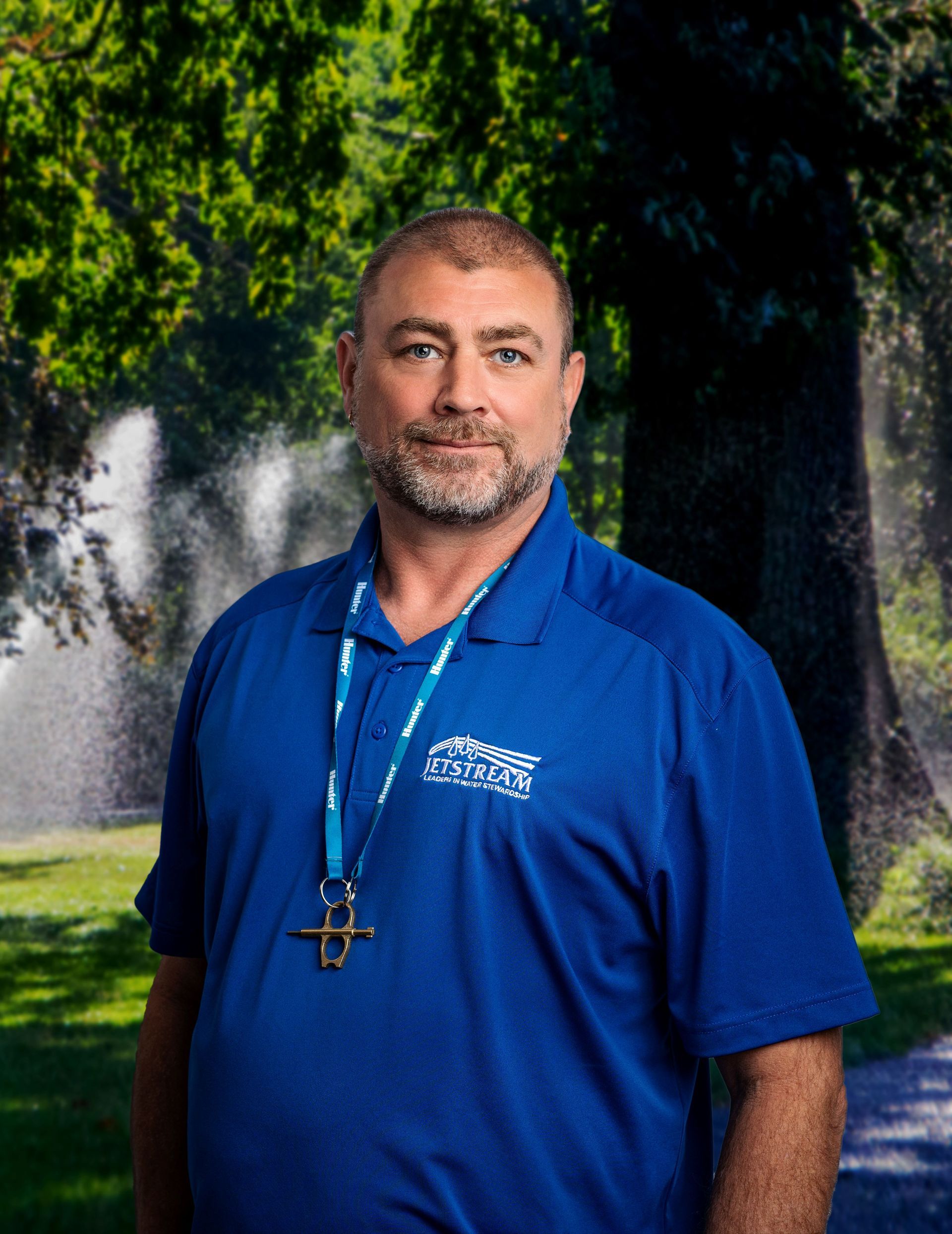 A man in a blue shirt is standing in front of a tree.