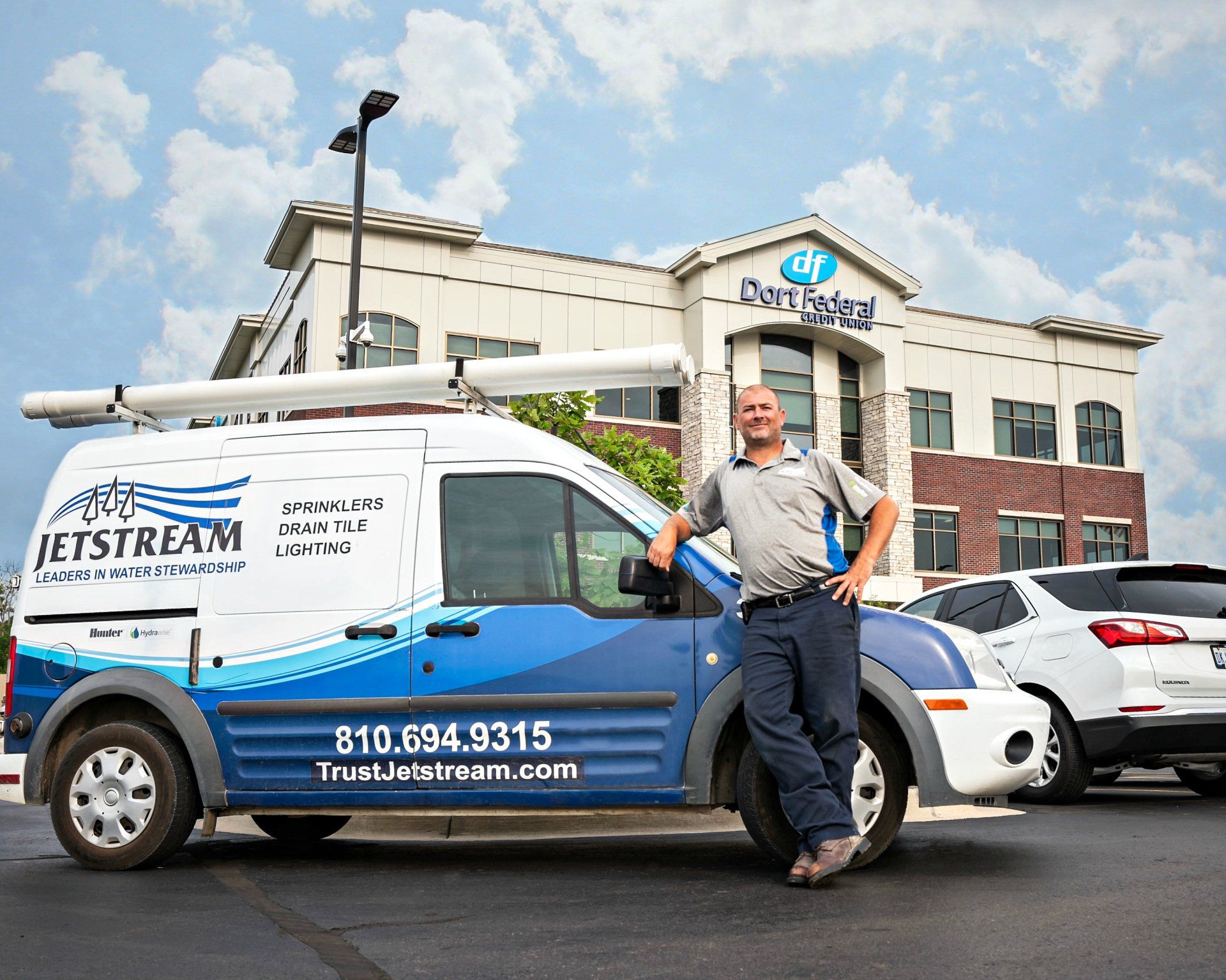 A man is standing next to a jetstream van in front of a building.