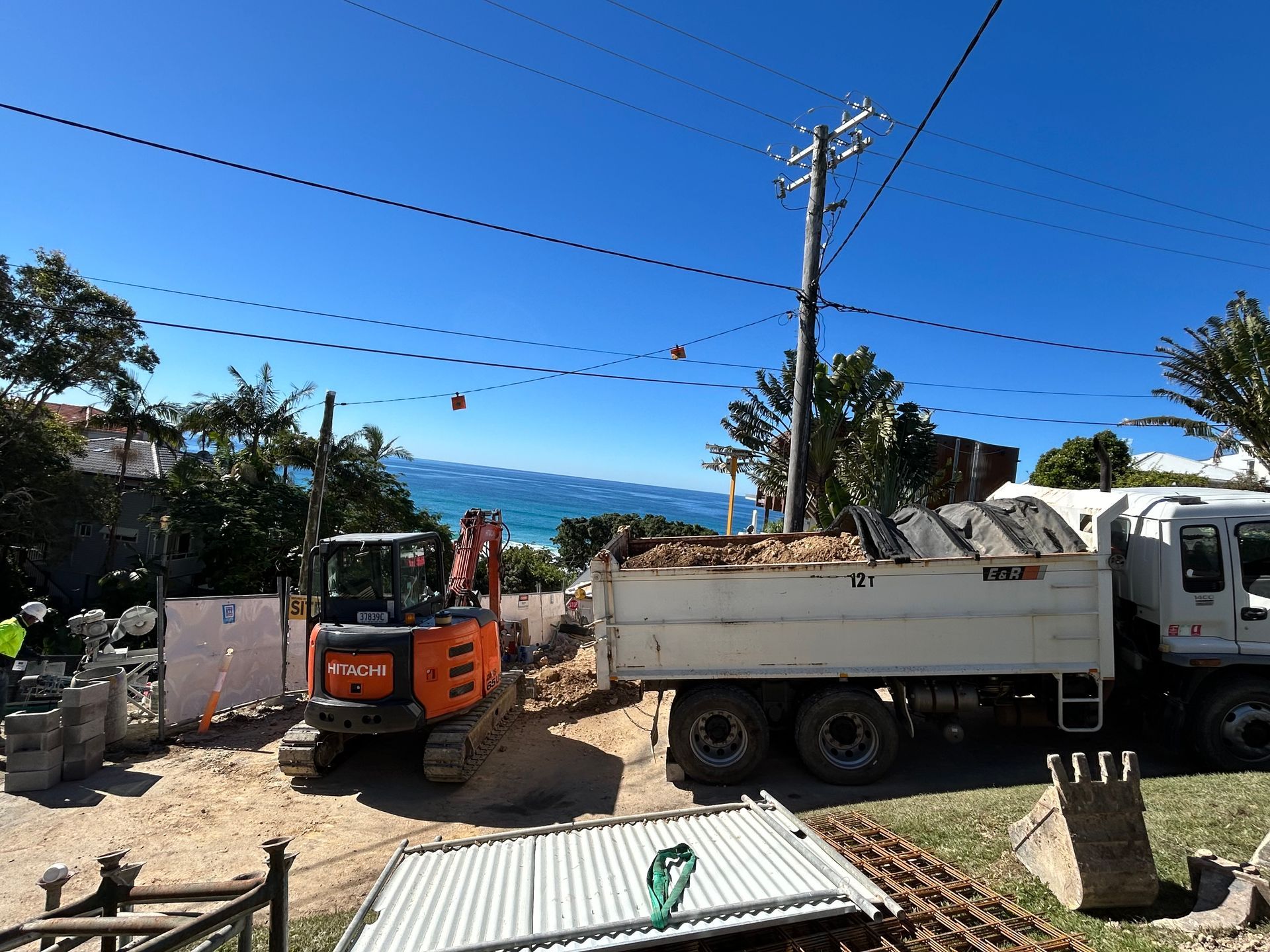 Construction trucks and debris in a sunny outdoor lot with mountains in the background