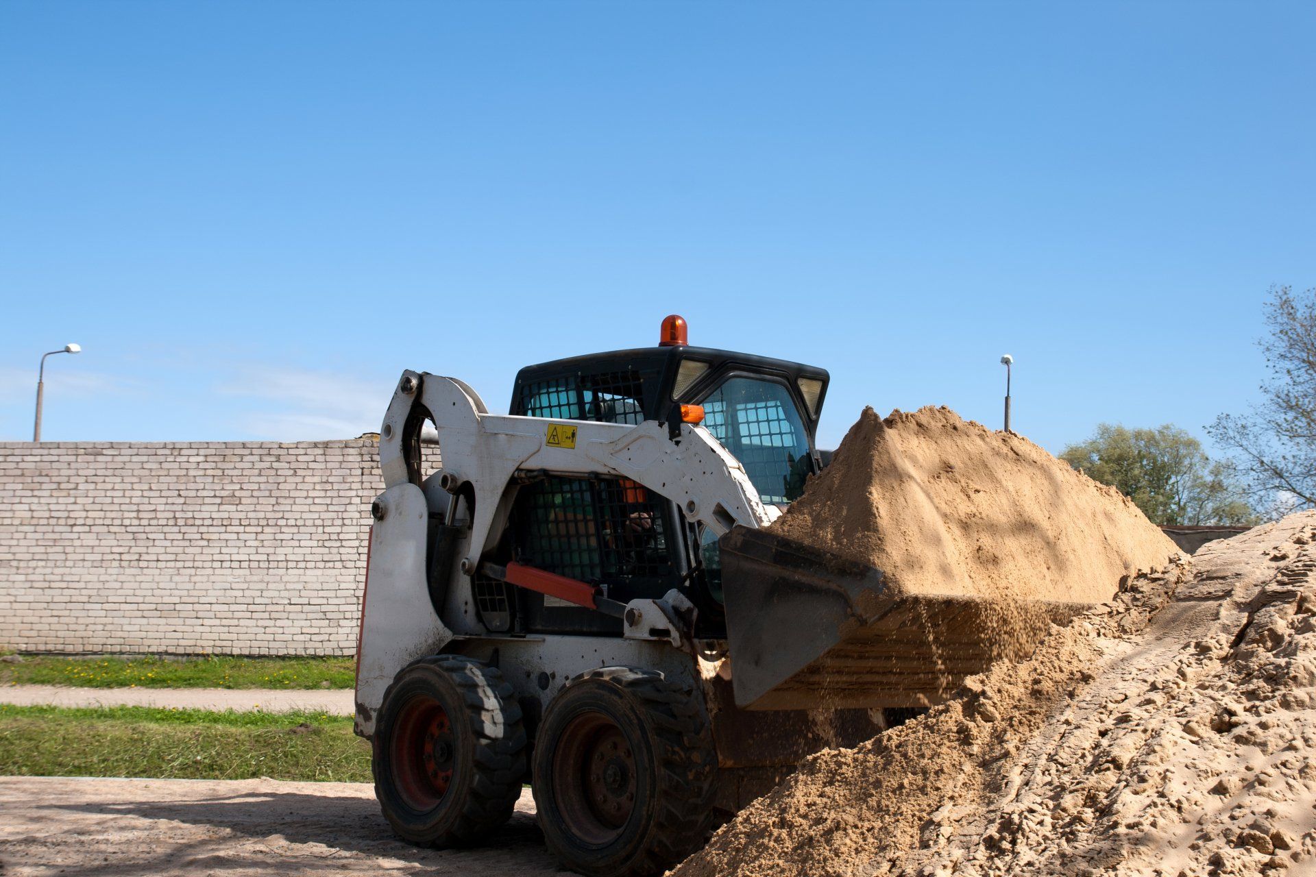 Front-end loader carrying a mound of sand at a construction site under a clear blue sky