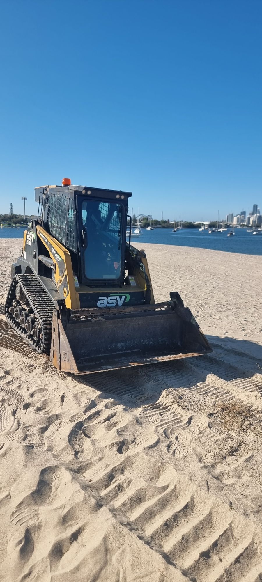 Yellow bulldozer on a sandy beach near the water under a clear blue sky