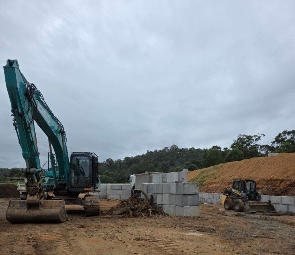 Excavators and stacked concrete blocks on a muddy construction site under cloudy sky