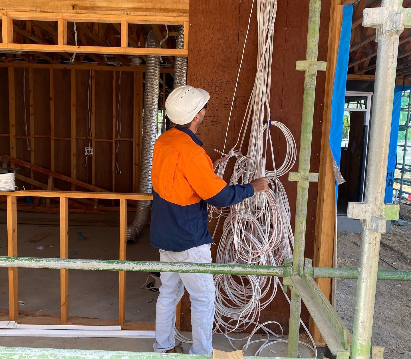 A Man Is Standing On A Scaffolding Holding A Bunch Of Wires  — Waltlec Industries In Garbutt, QLD