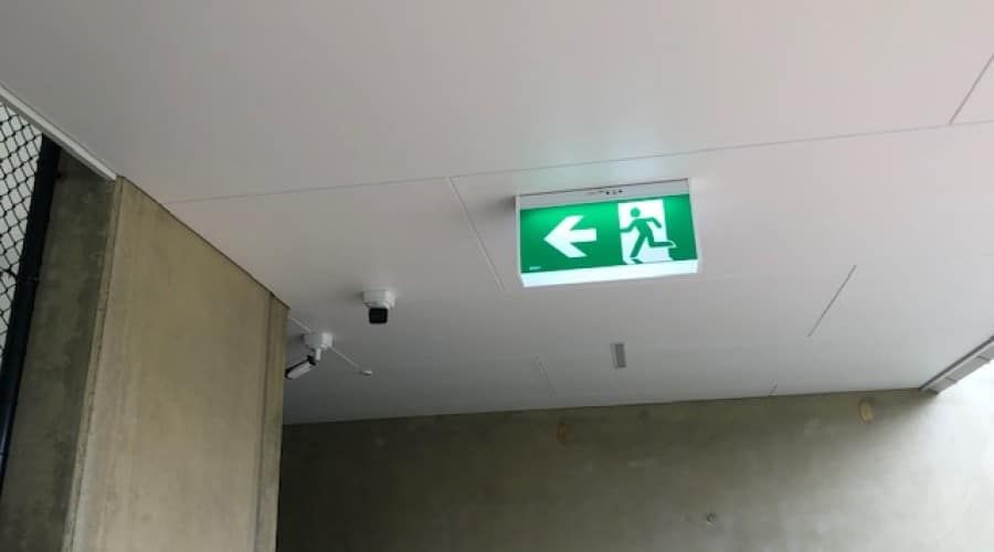 A Green Exit Sign Is Hanging from The Ceiling of A Building — Waltlec Industries In Garbutt, QLD