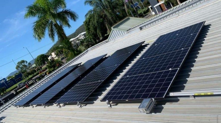 A Row of Solar Panels on A Roof with A Palm Tree in The Background — Waltlec Industries In Garbutt, QLD