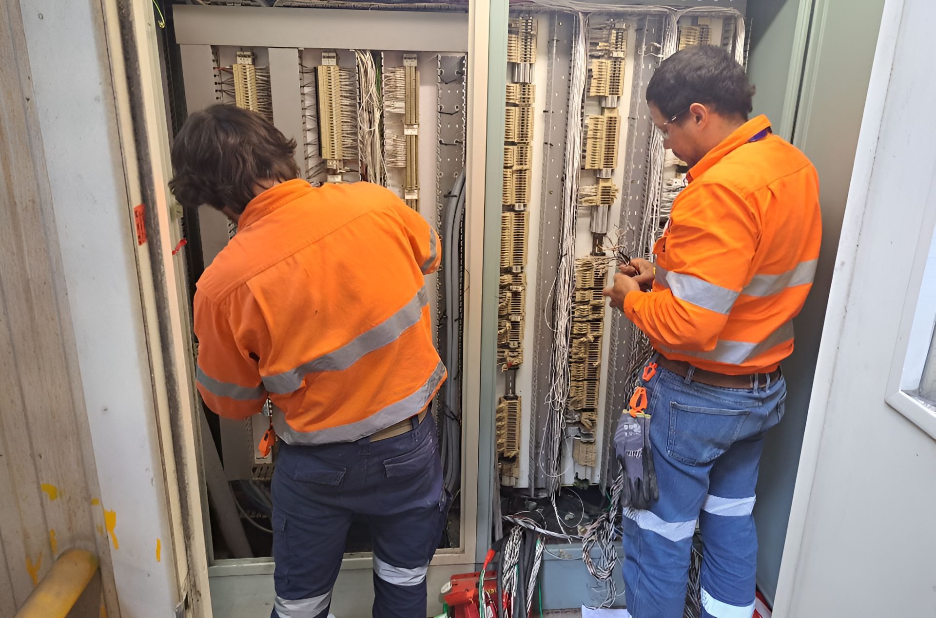 Two Men In Orange Shirts Are Working On A Electrical Box  — Waltlec Industries In Garbutt, QLD
