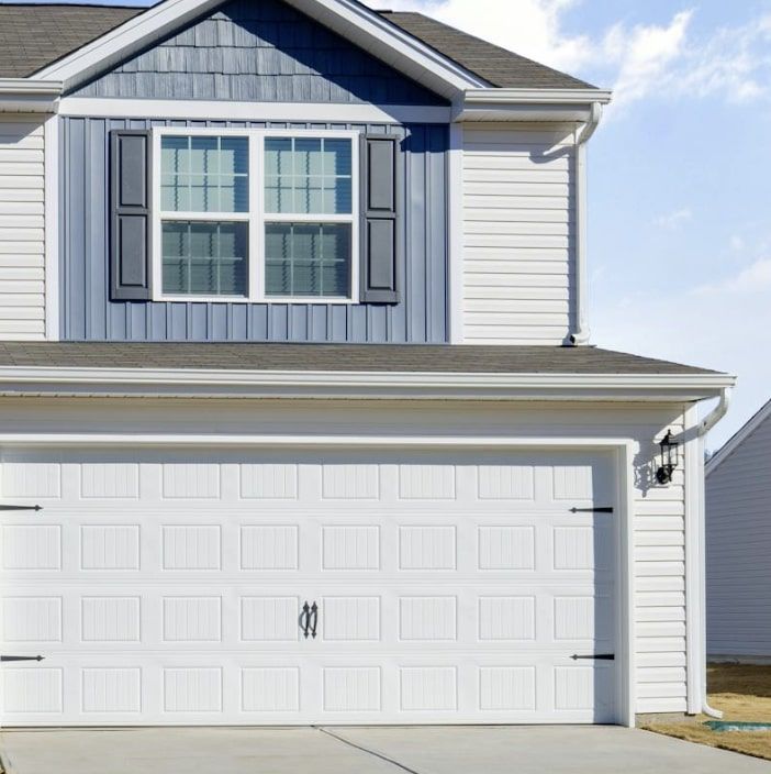A white house with blue and white Vinyl siding and a white garage door