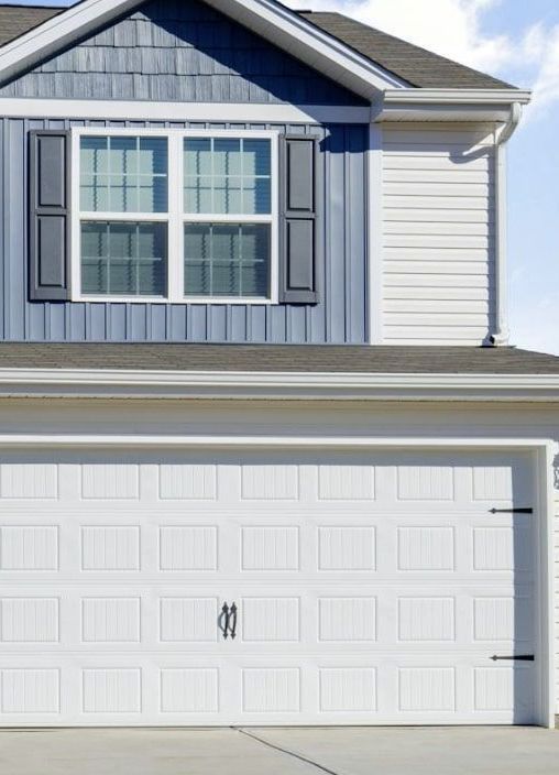 A white house with blue and white Vinyl siding and a white garage door