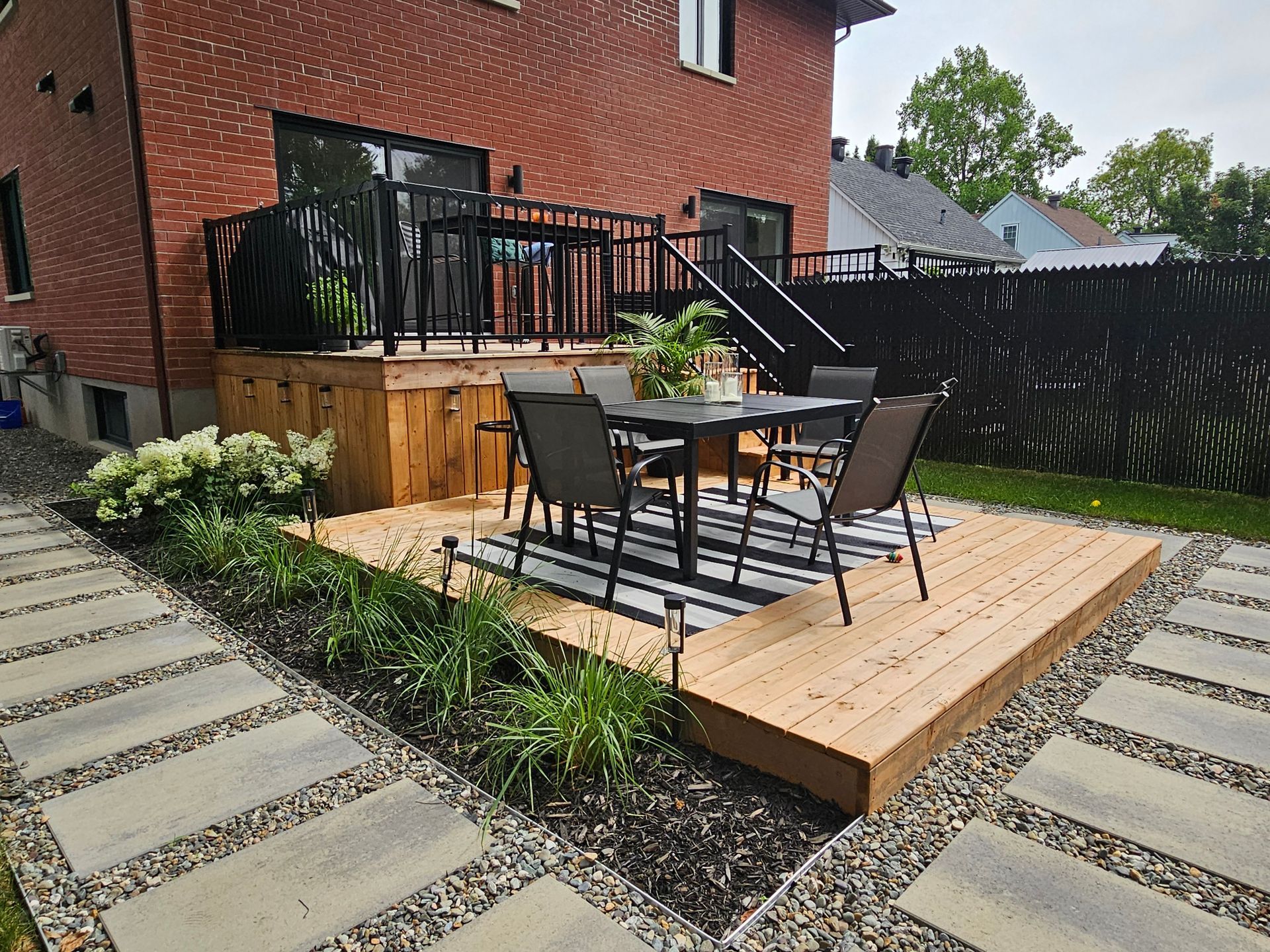 Une terrasse en bois avec une table et des chaises devant une maison en briques.