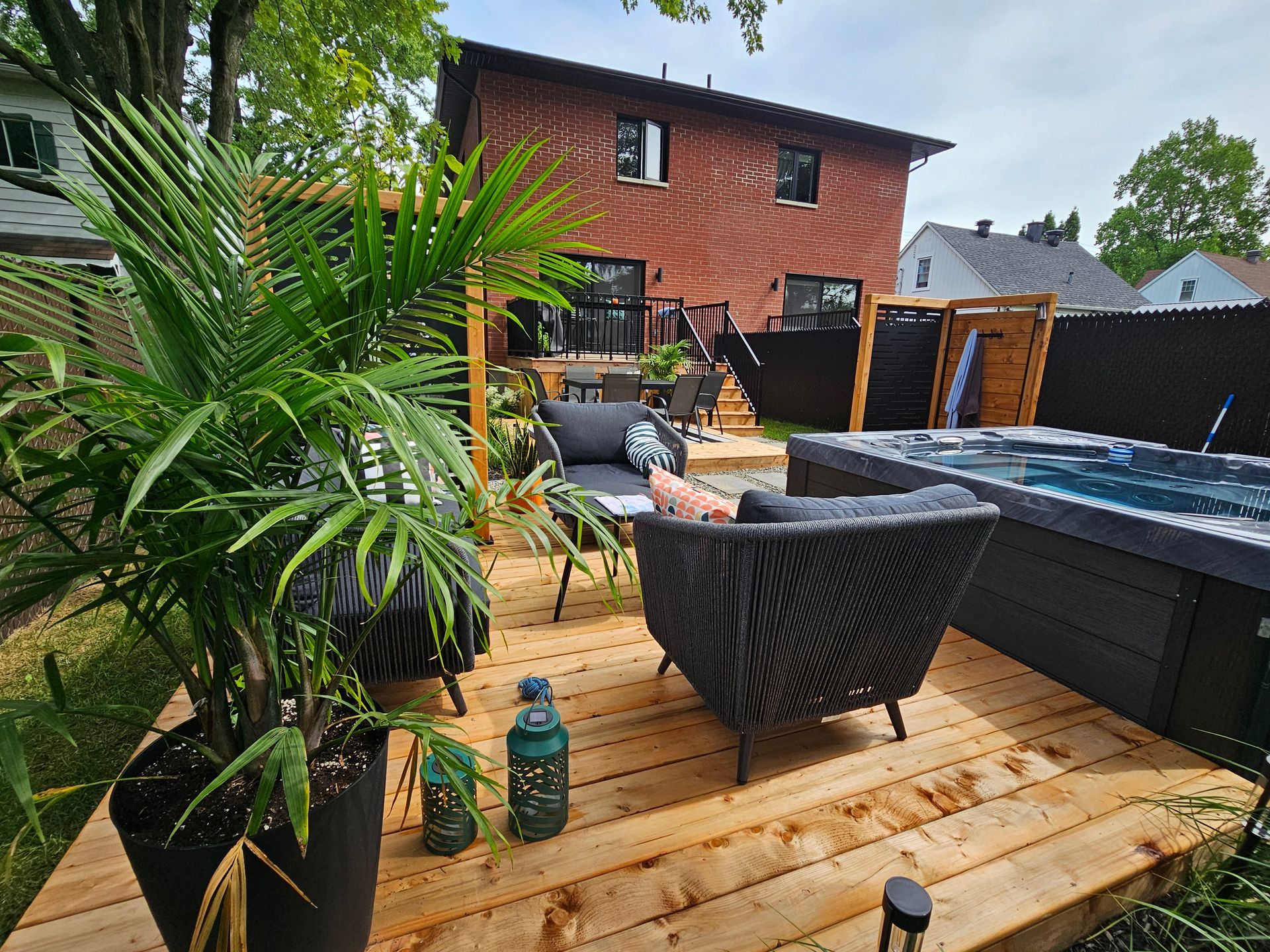 Une terrasse en bois avec un bain à remous et des chaises devant une maison en briques.