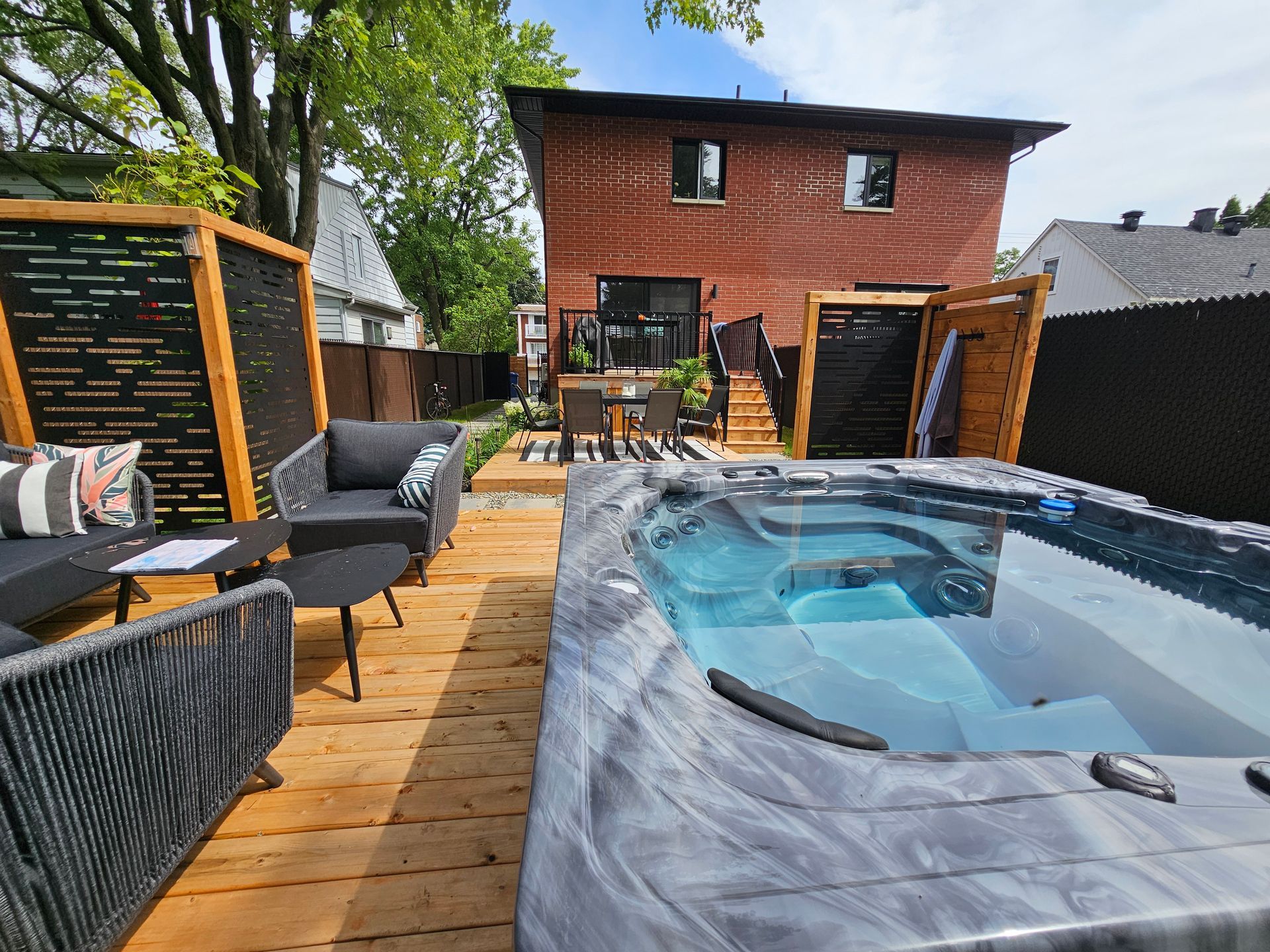 Un bain à remous est installé sur une terrasse en bois devant une maison en briques.