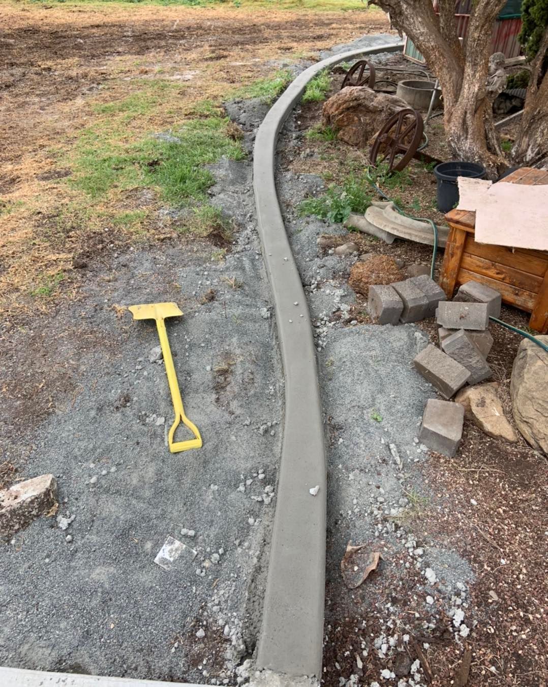 A Yellow Shovel is Sitting Next to a Concrete Curb — Pedro's Concreting in Pittsworth, QLD