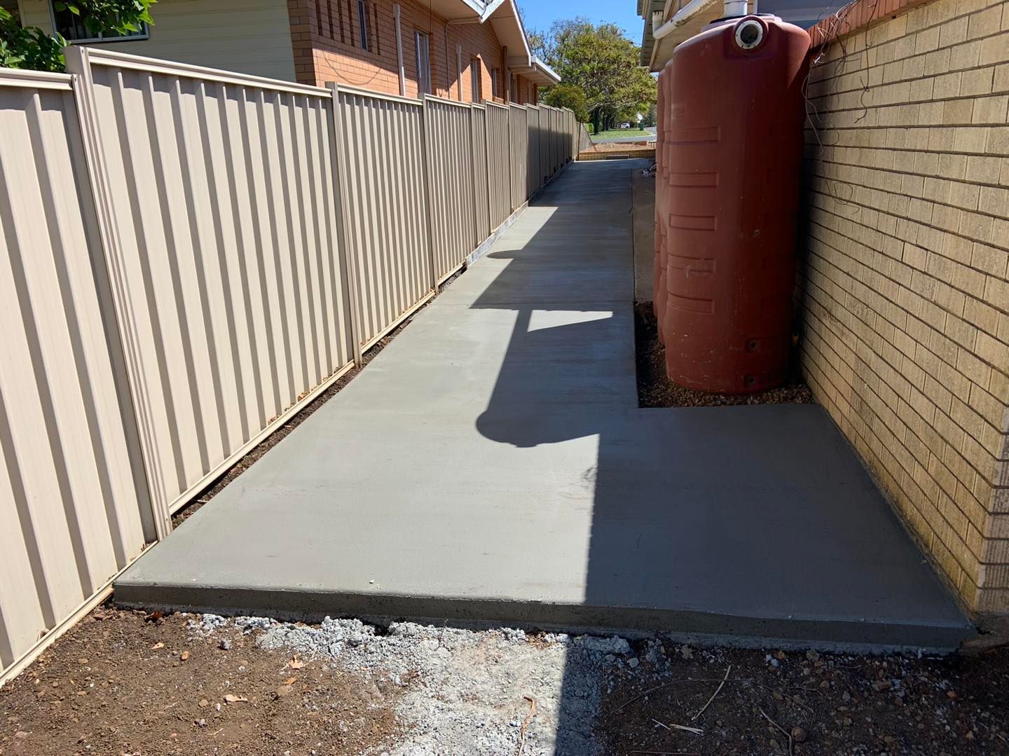 A Concrete Walkway Leading to a Water Tank Next to a Brick Wall — Pedro's Concreting in Pittsworth, QLD