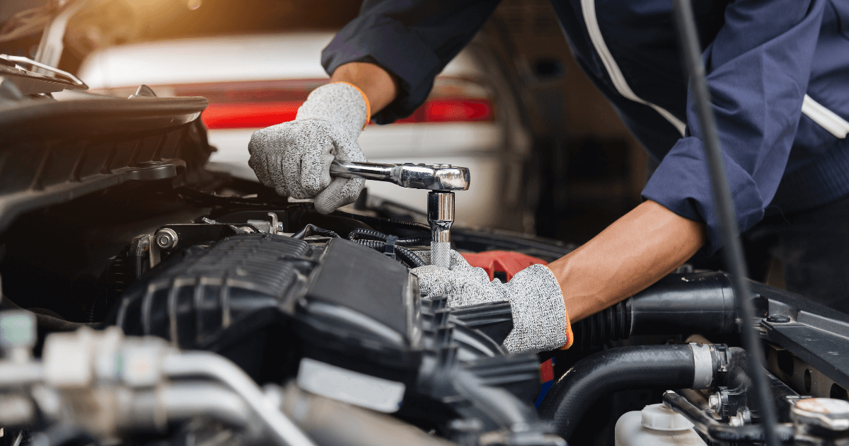 a mechanic under the hod of a car holding a light