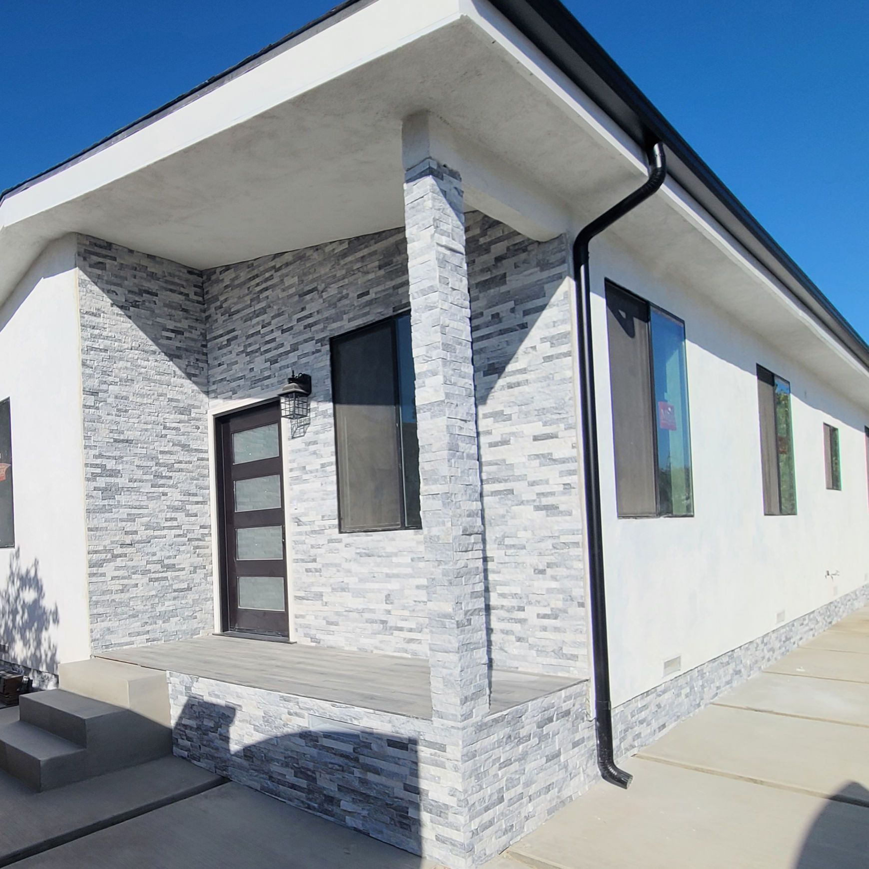 A white house with a stone facade and a black gutter