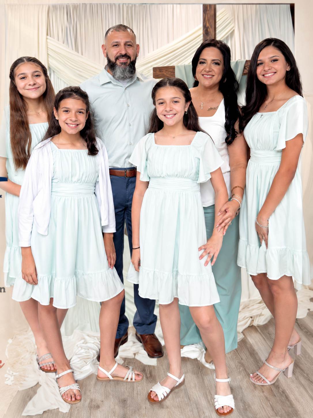 Family of six standing together indoors, wearing coordinated light blue and white outfits, smiling at the camera.