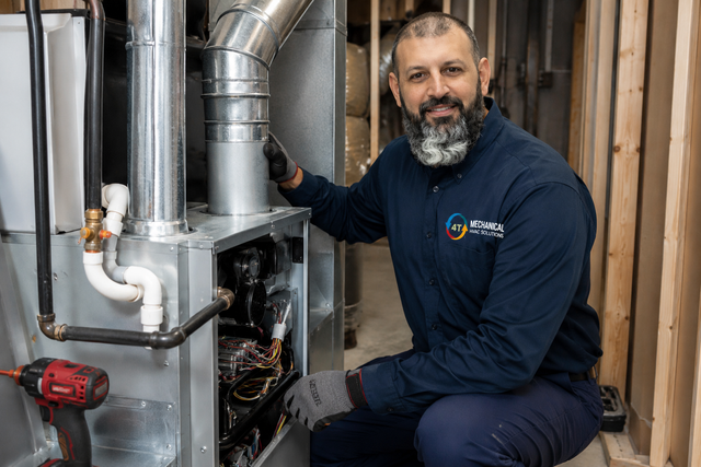 Technician kneeling beside a furnace, inspecting HVAC equipment in a utility room