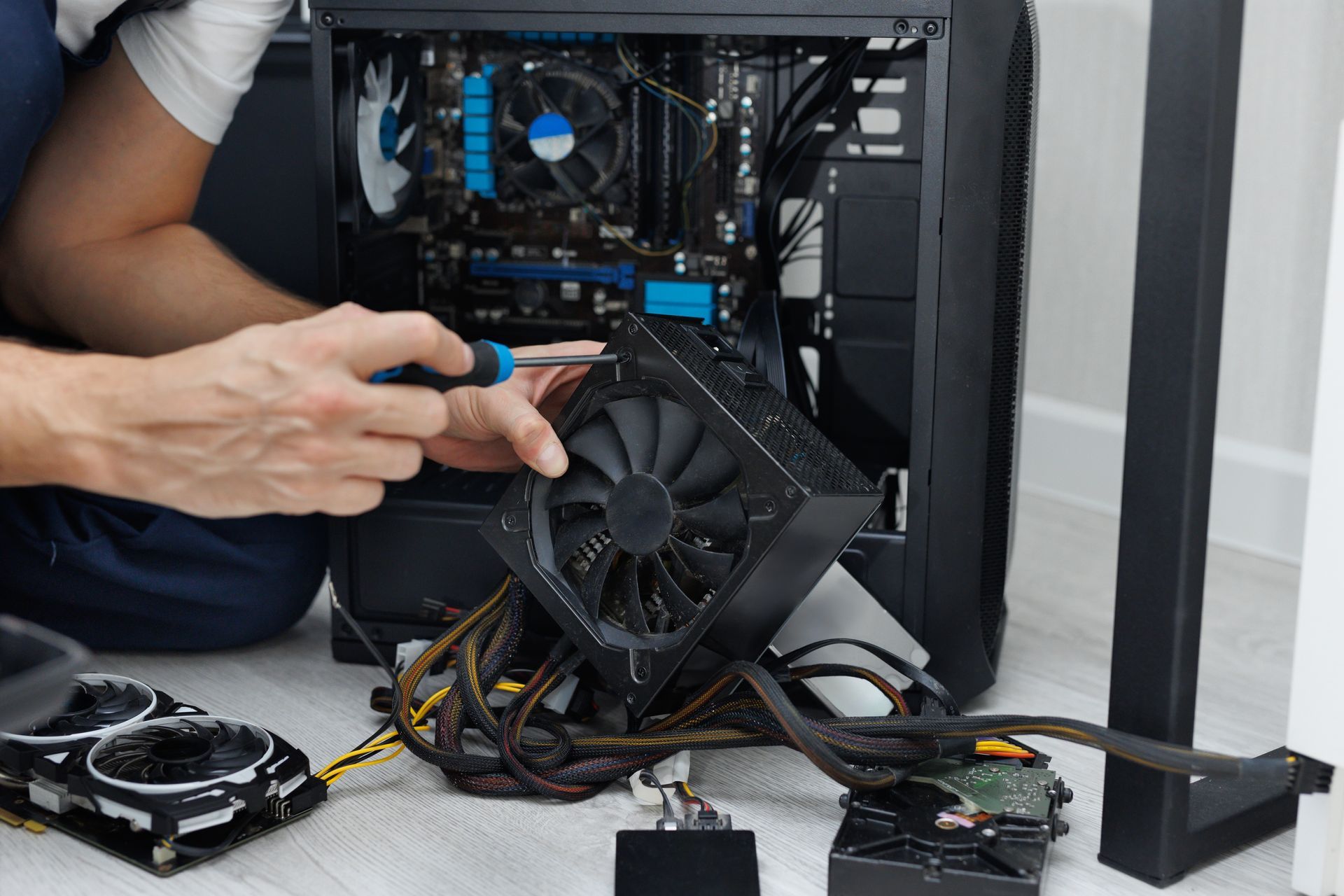 Person installing a graphics card inside a desktop PC tower, with tools and loose cables on the floor.