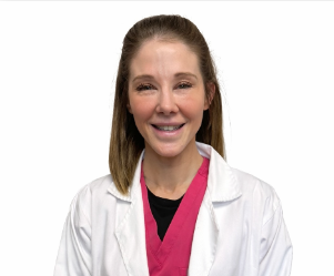 Woman in white lab coat smiles, wearing pink top, against white background.