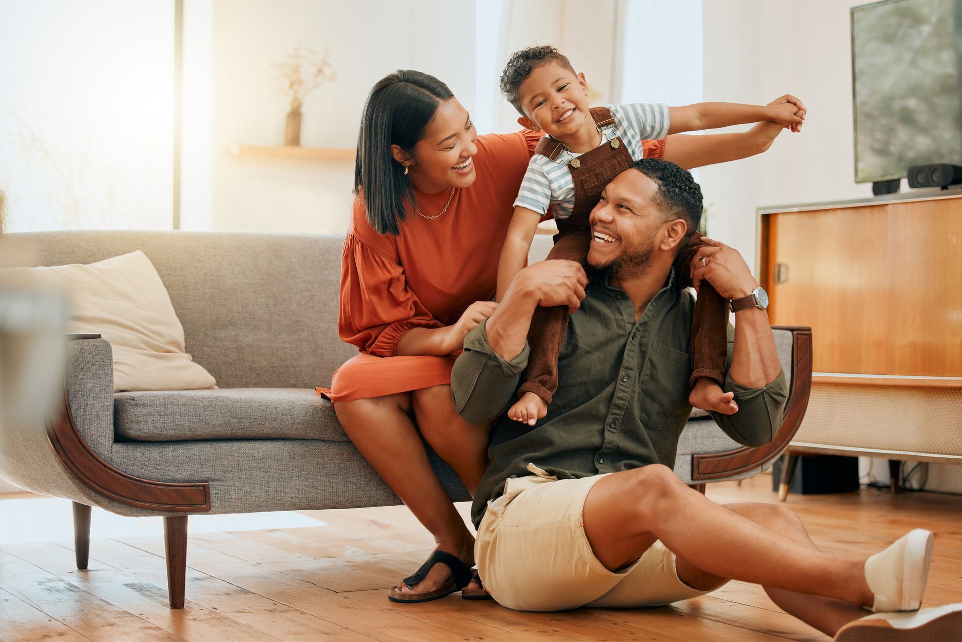Family laughing together on a living room couch, with a child playfully hugging the adults.