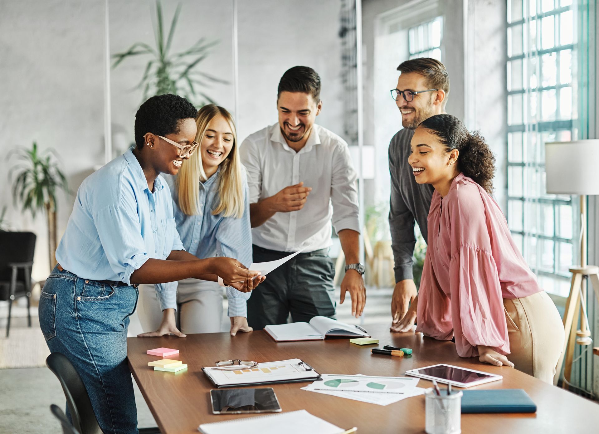 Group of coworkers collaborating around a table in a bright office, reviewing papers and smiling.