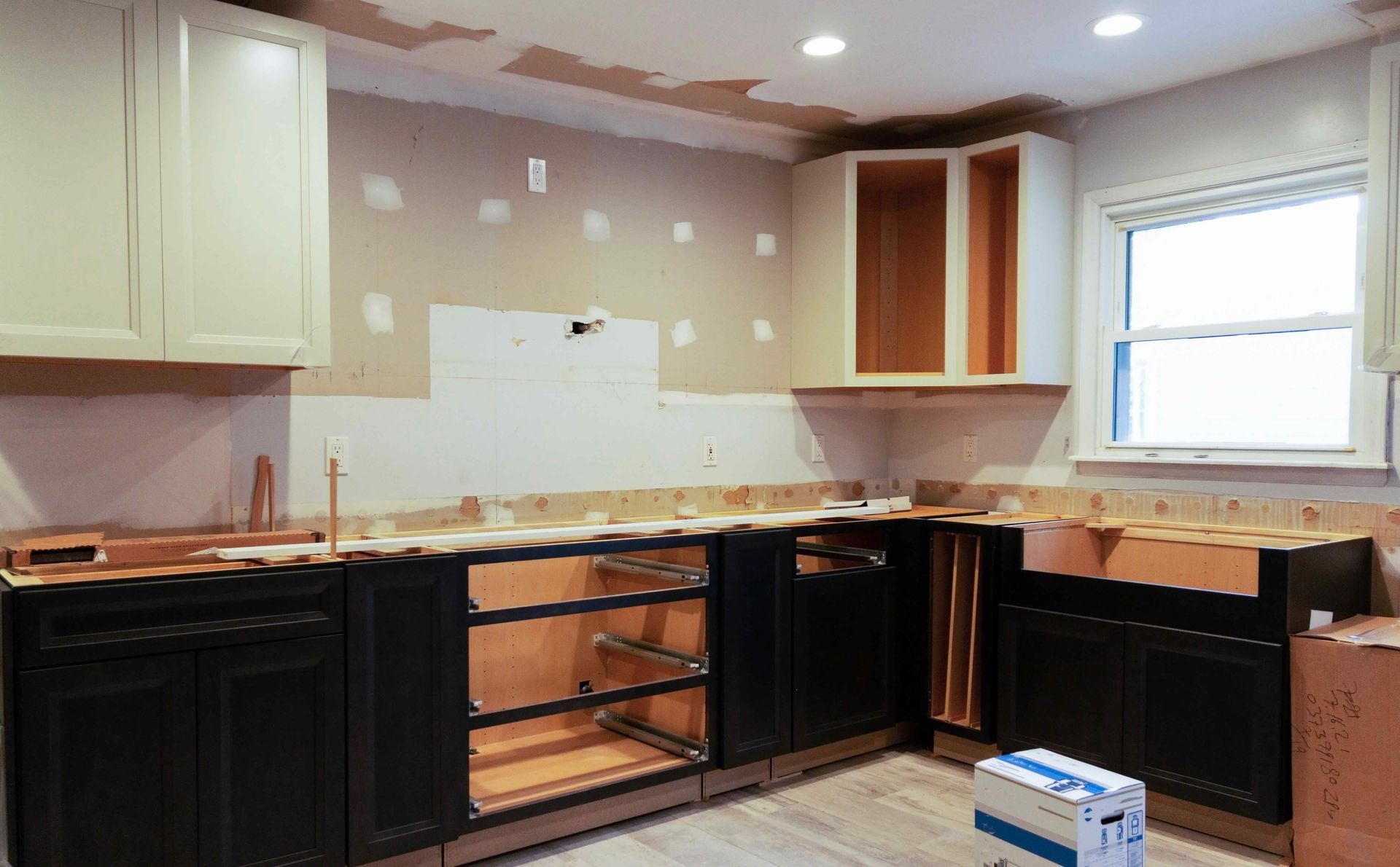 Kitchen renovation: black base cabinets, cream upper cabinets, bare walls, countertop, and window.