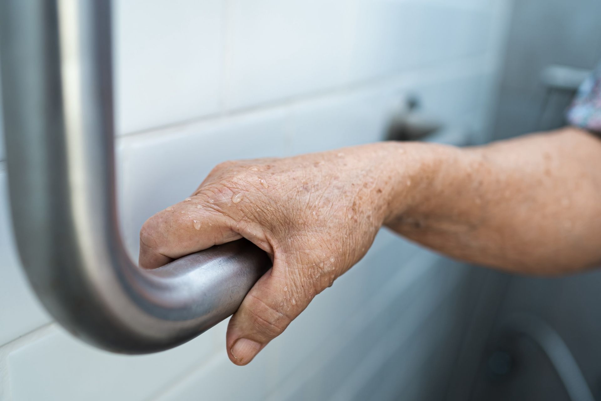An elderly woman is holding onto a metal railing in a bathroom.