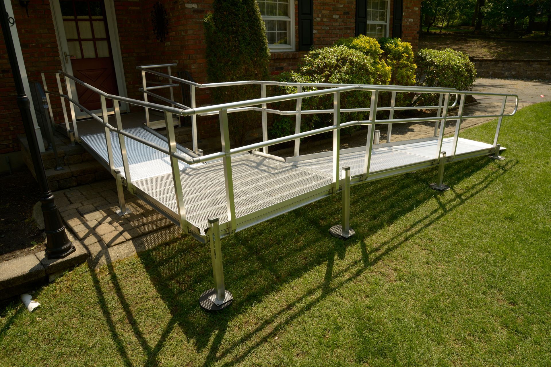 Elevated metal wheelchair ramp with railings beside a brick building over a grassy lawn