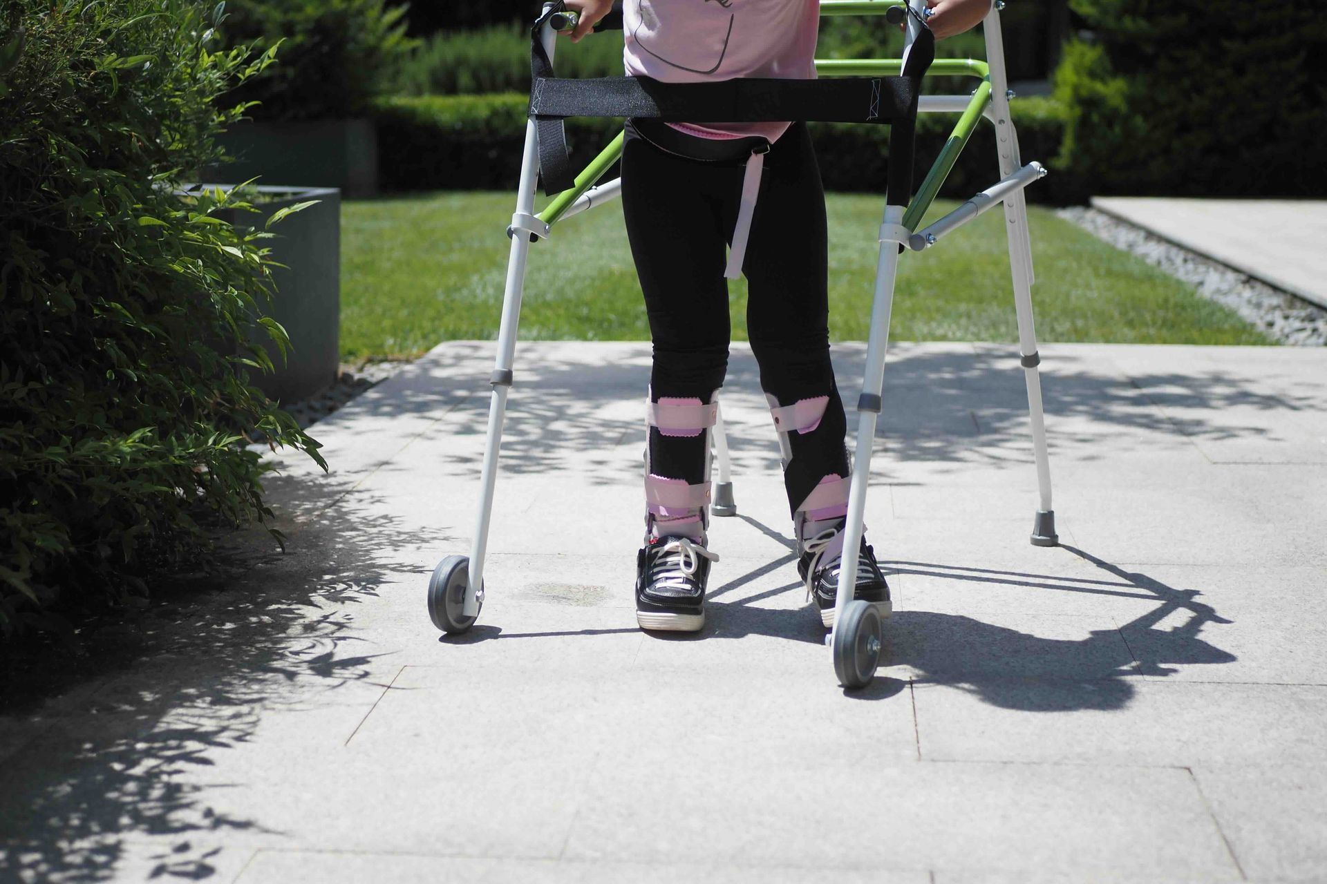 A little girl is walking with a walker on a sidewalk.