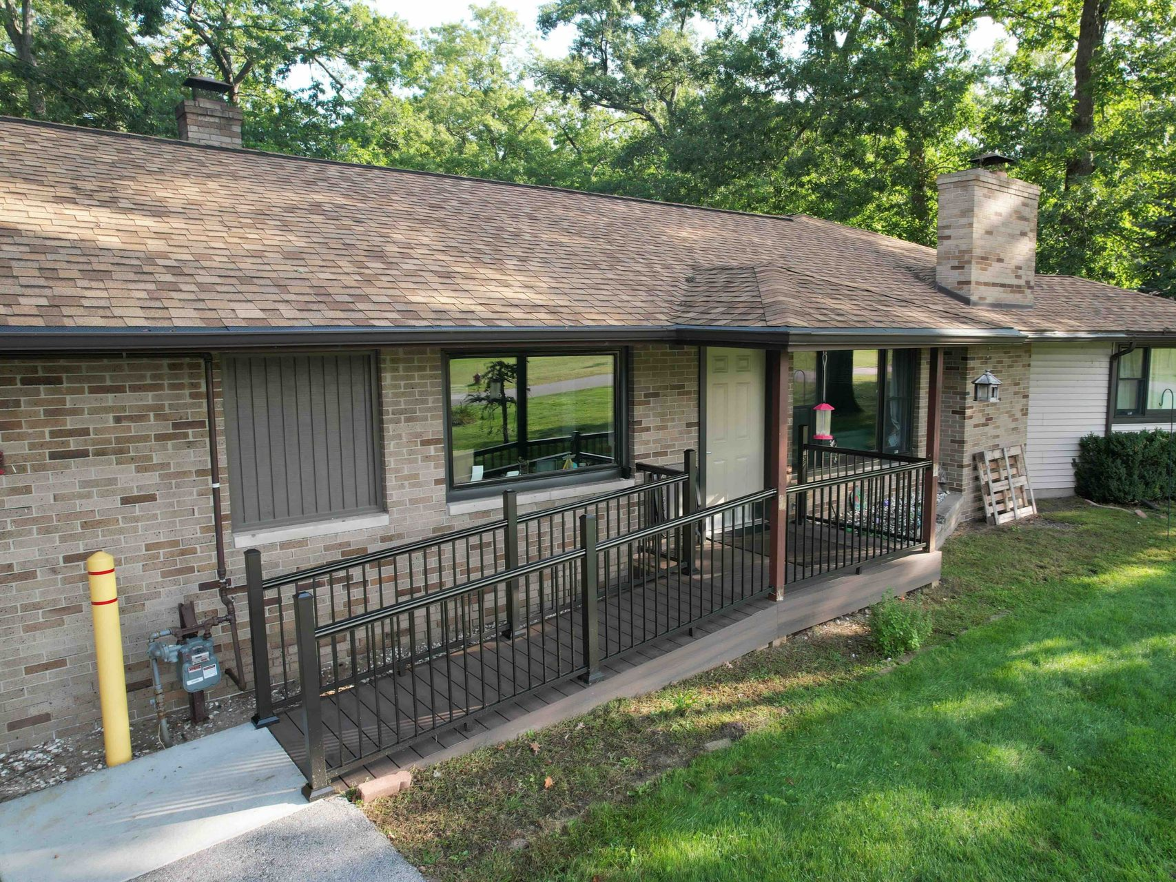 Ramp leading to a brick building's entrance. Black railing, brown roof, and green lawn.