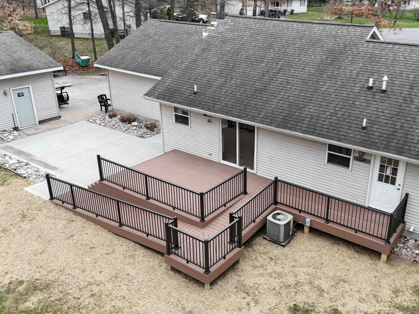 Elevated composite deck with black railings and brown steps, attached to a light-colored house.