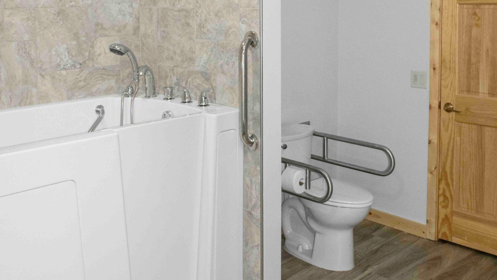 Accessible bathroom featuring a white walk-in bathtub with a grab bar and a toilet equipped with safety support rails.