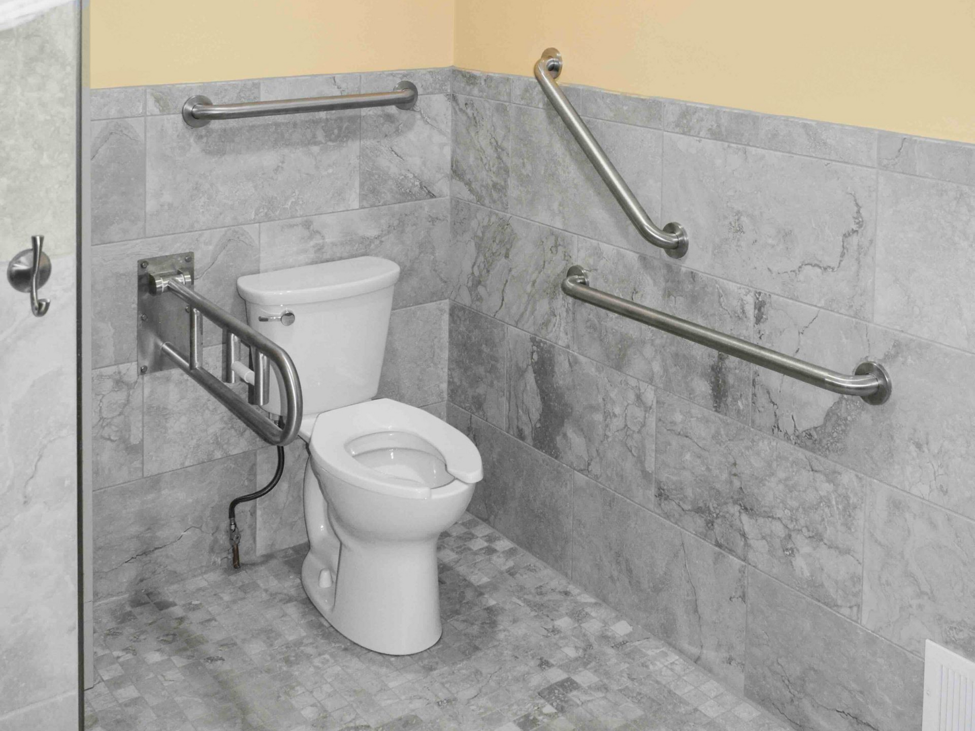 Accessible bathroom with toilet and grab bars on a gray tiled wall.