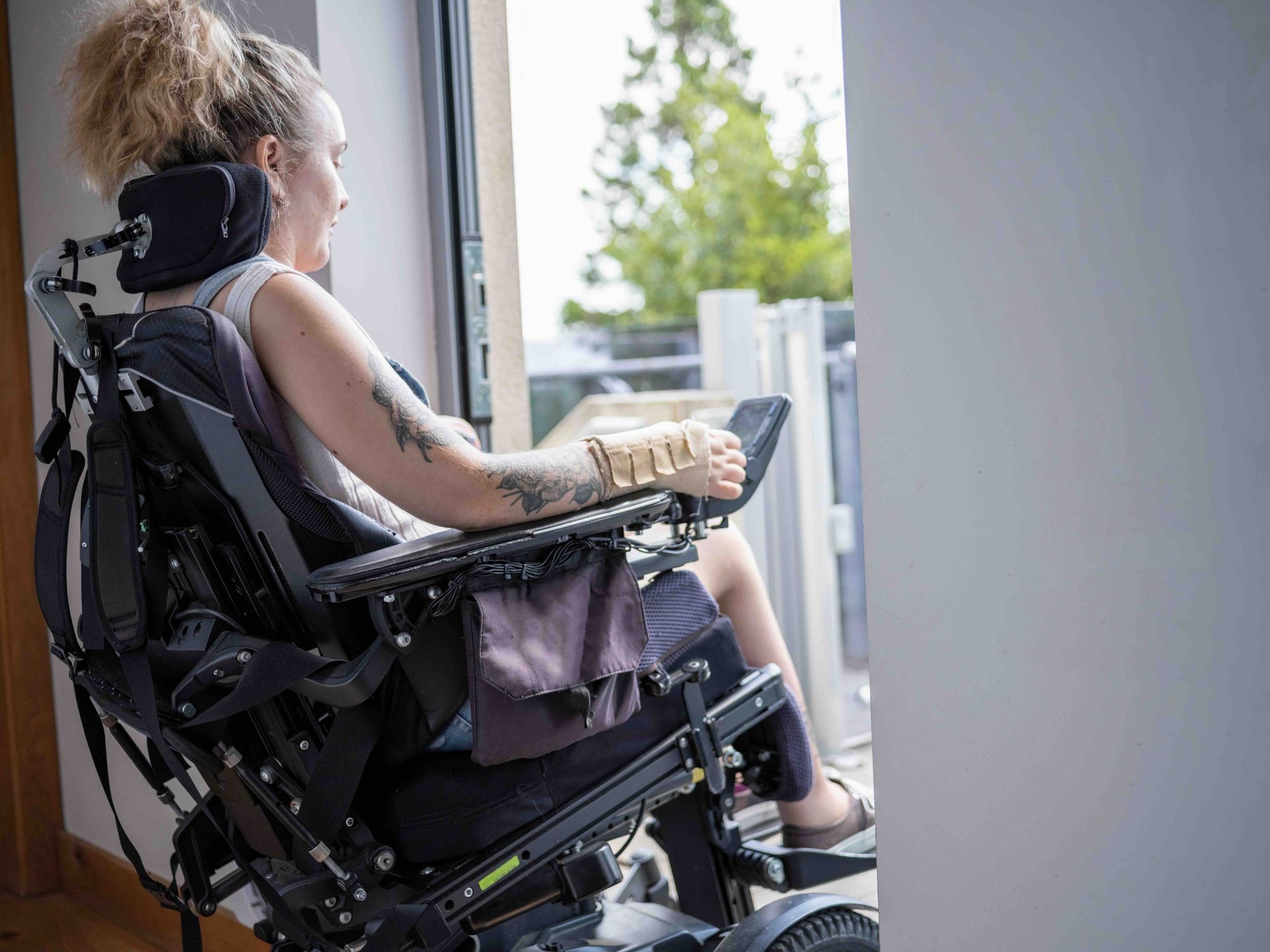 A woman in a power wheelchair looking out a window, smilingoing through  a home entryway.