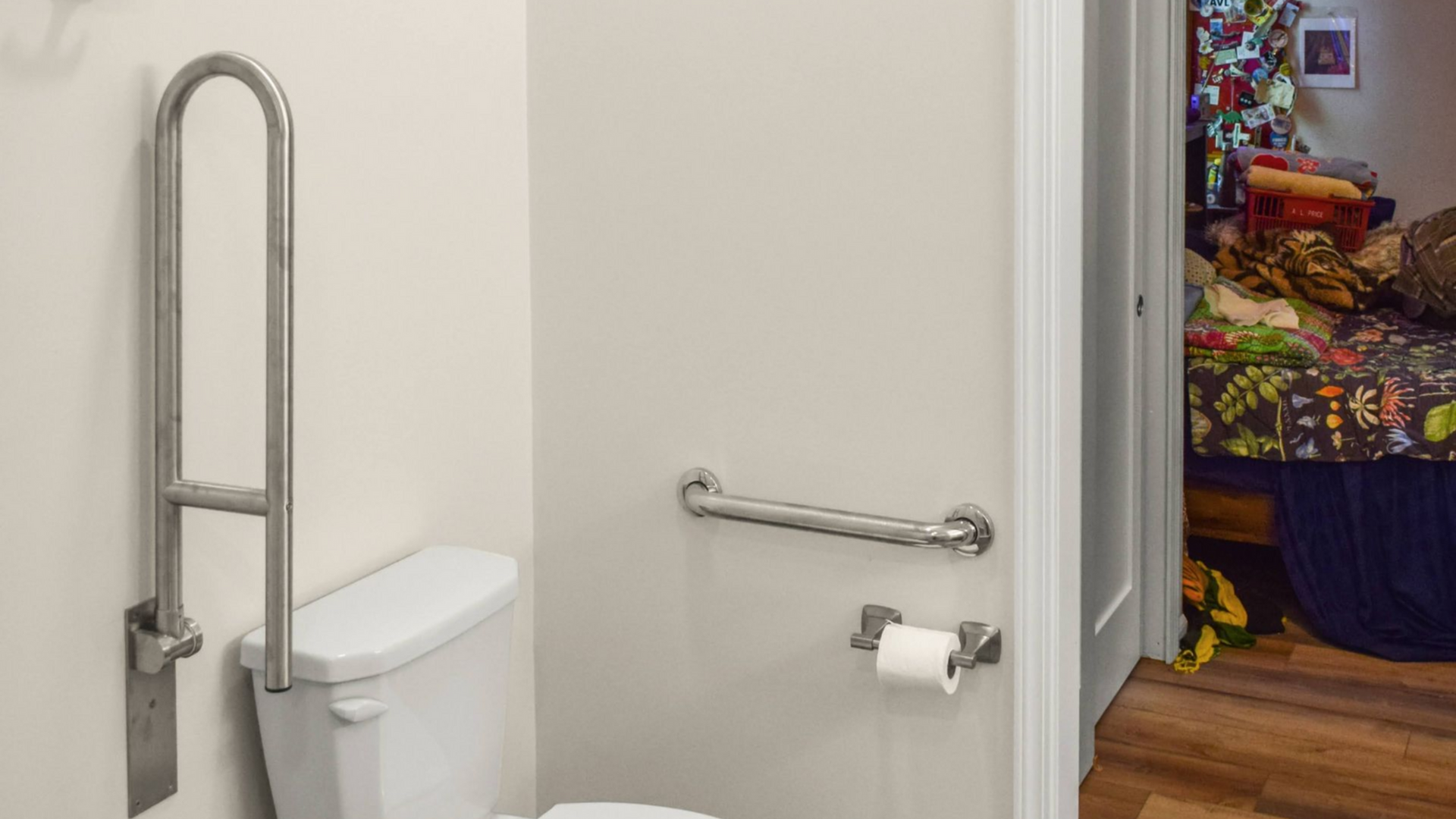 Accessible bathroom stall featuring a toilet with a drop-down grab bar and a wall-mounted grab bar above toilet paper.