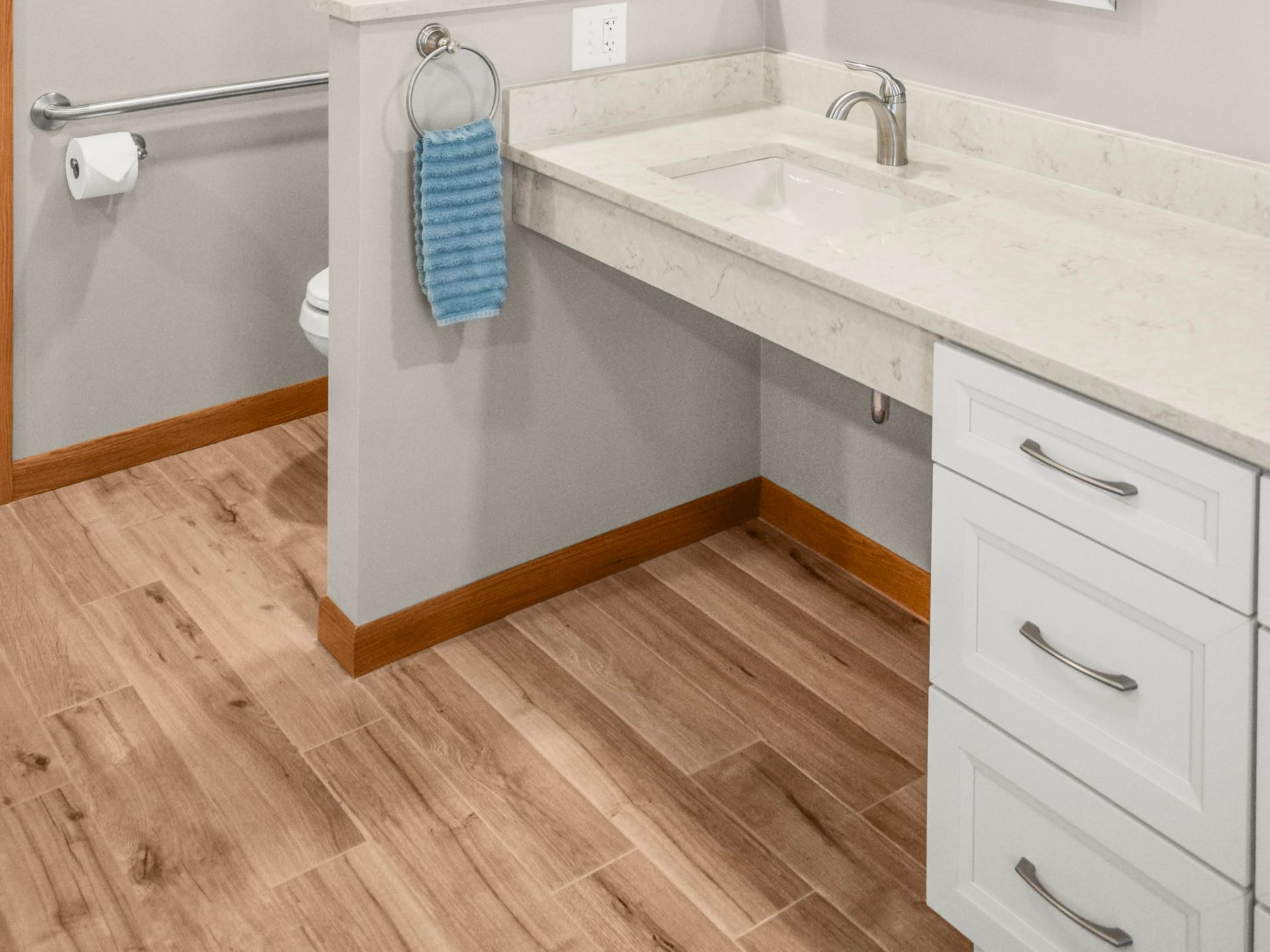 Bathroom with a light countertop, white cabinets, wood-look floor, and accessible sink area with a grab bar.