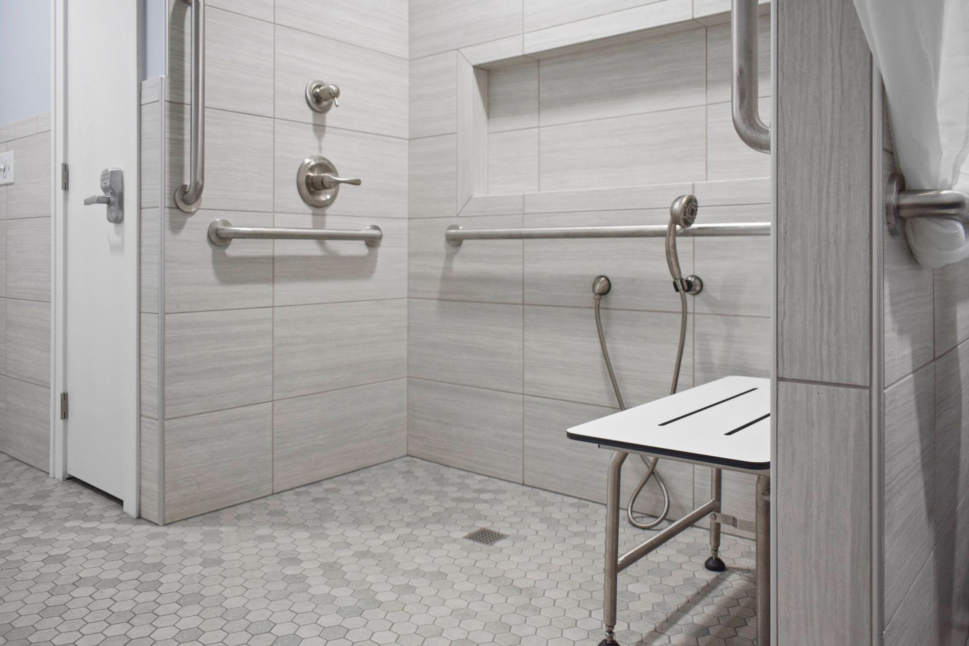 Accessible shower with grab bars and a seat, tiled walls and floor.