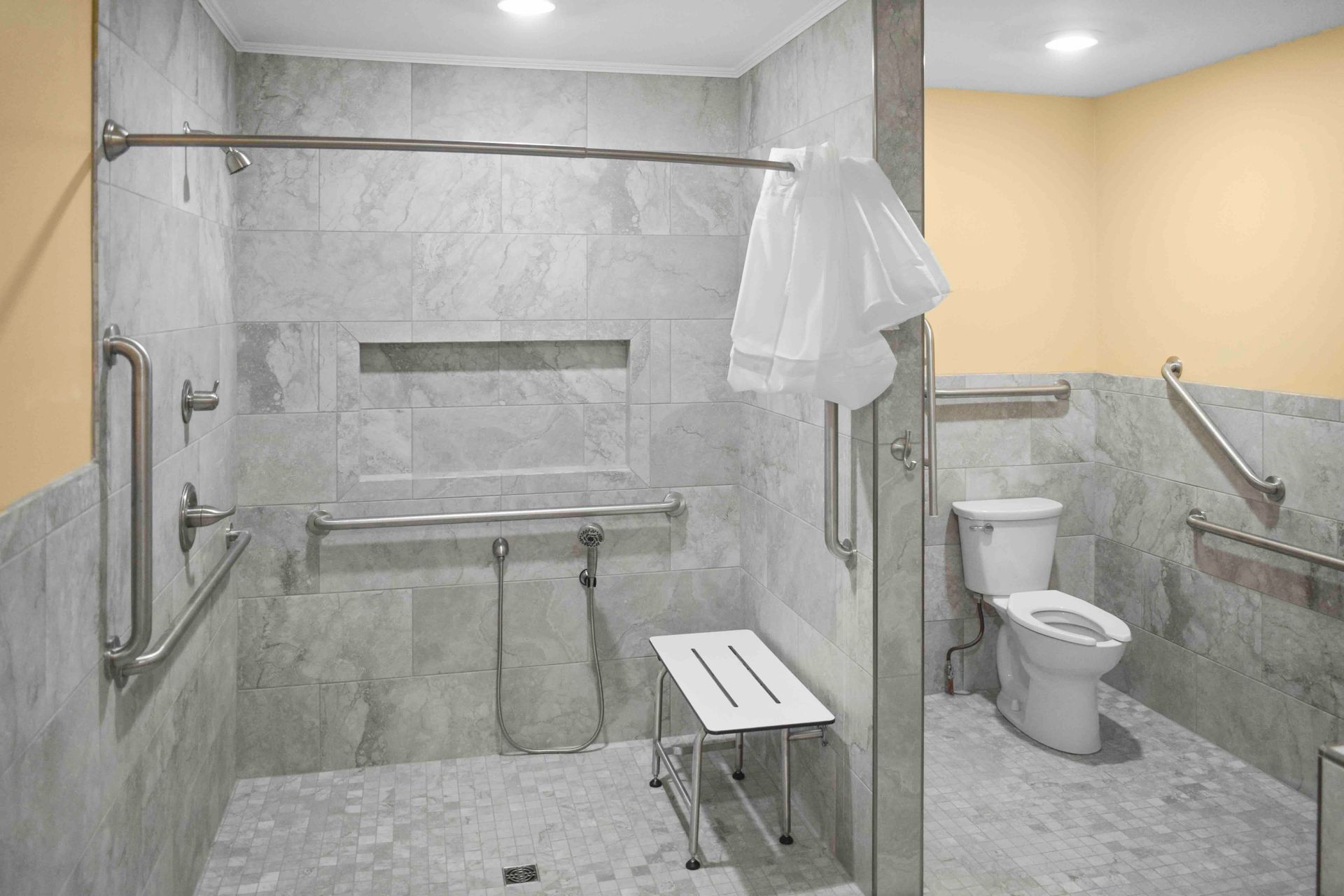 A bathroom with a toilet , shower , and bench.