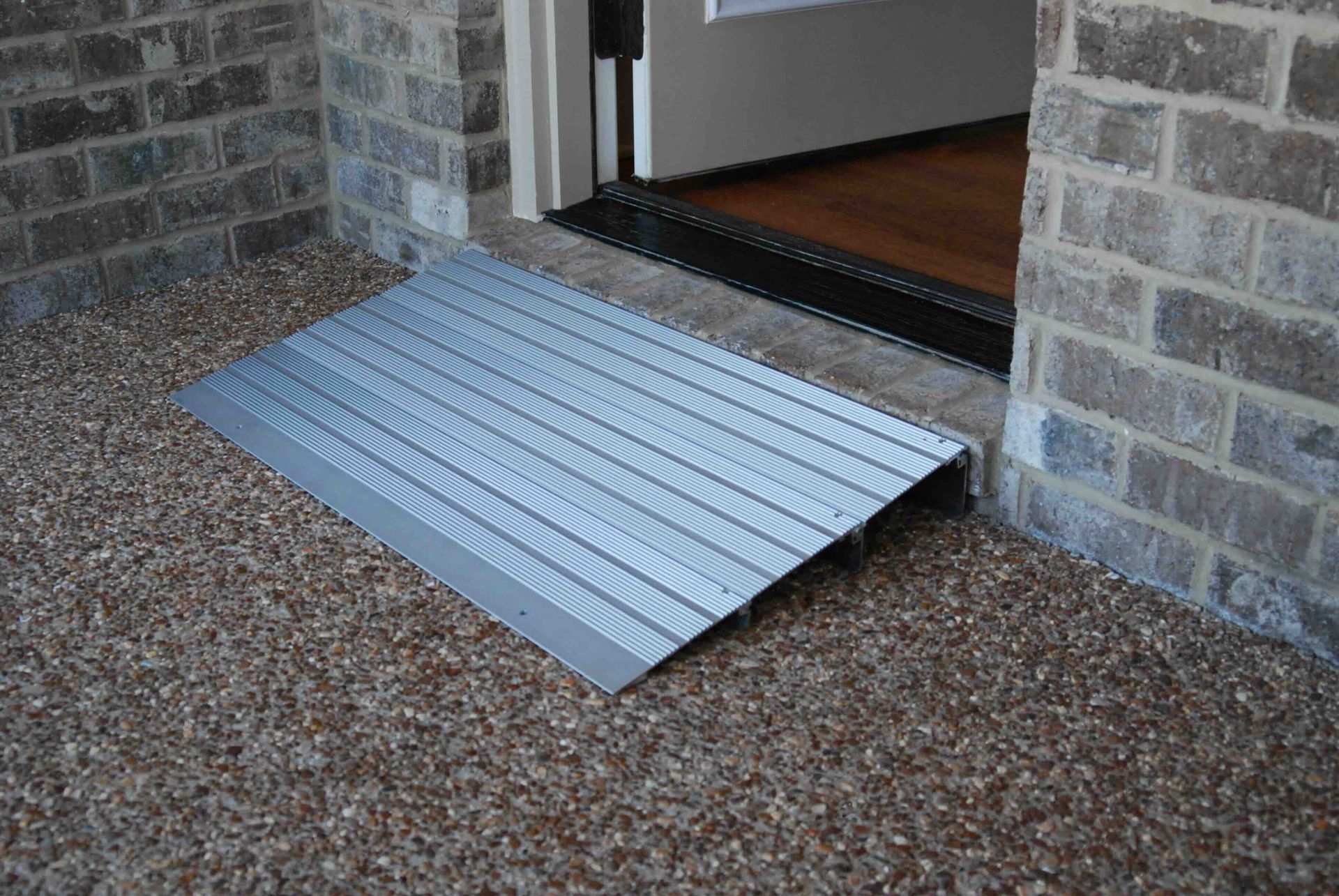 A metal wheelchair doorway ramp is sitting in front of a brick door.