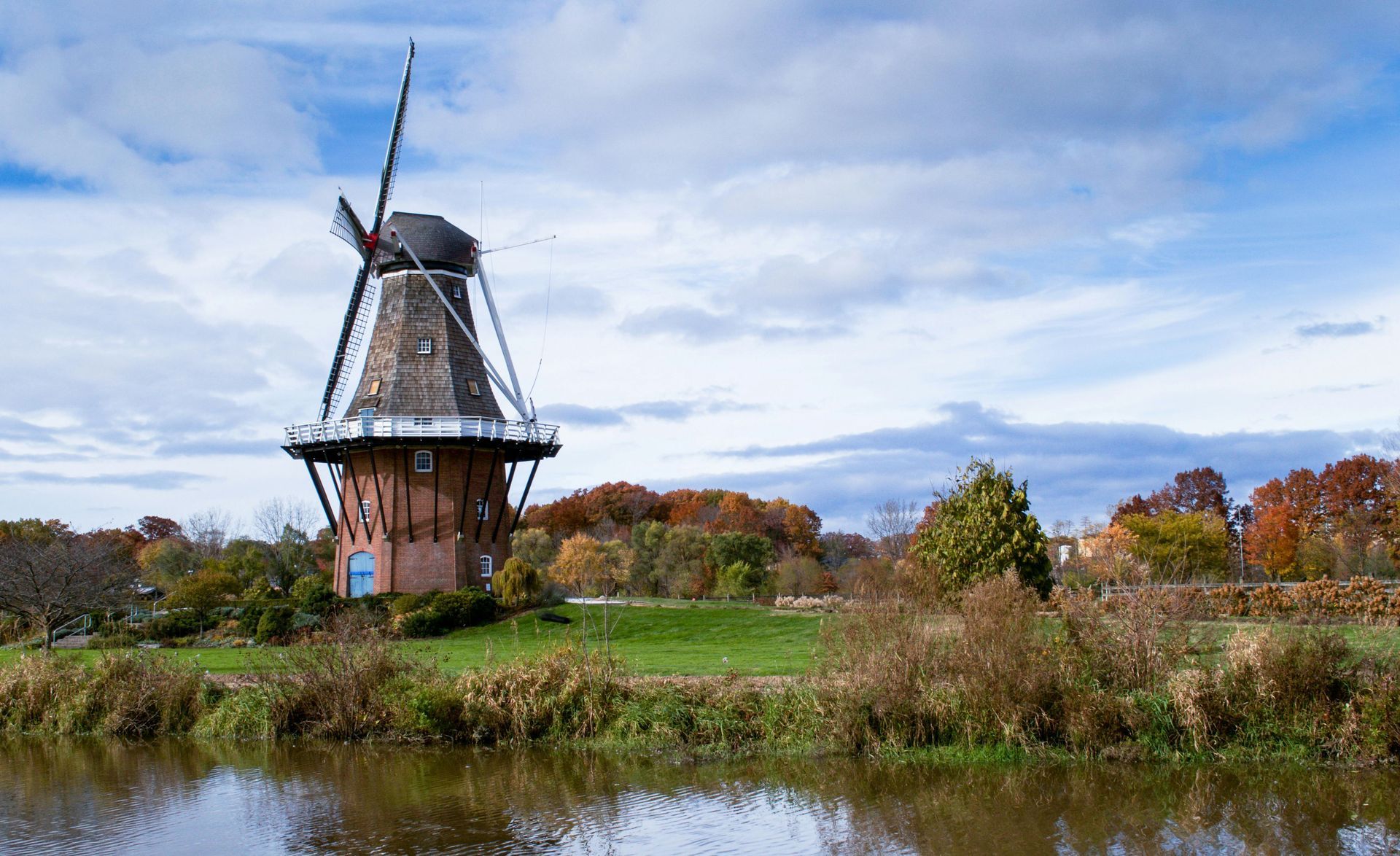 A windmill is sitting on top of a grassy hill next to a river in Holland, Michigan.
