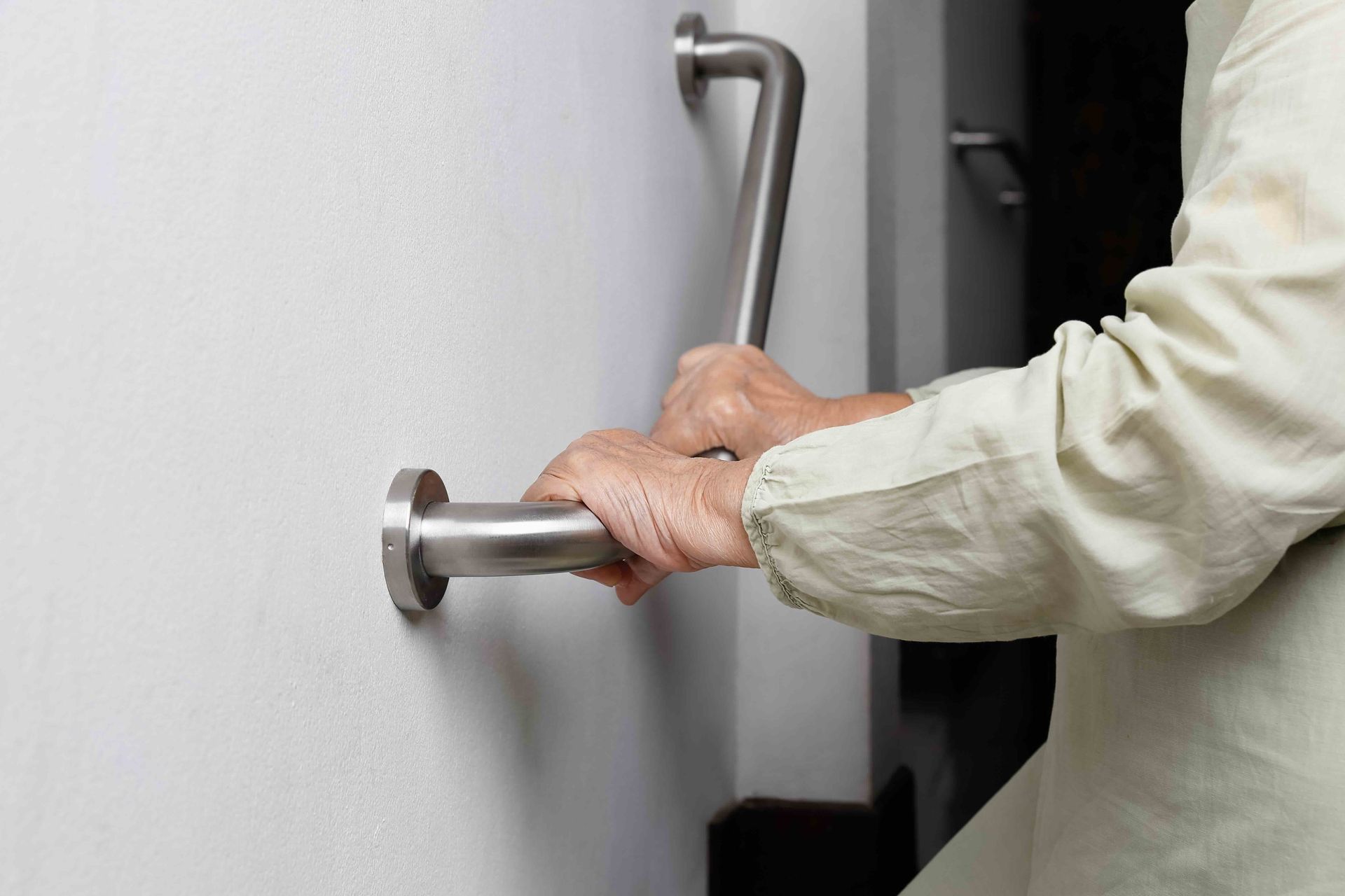 A person’s hands gripping a metal safety grab bar installed on a white wall.