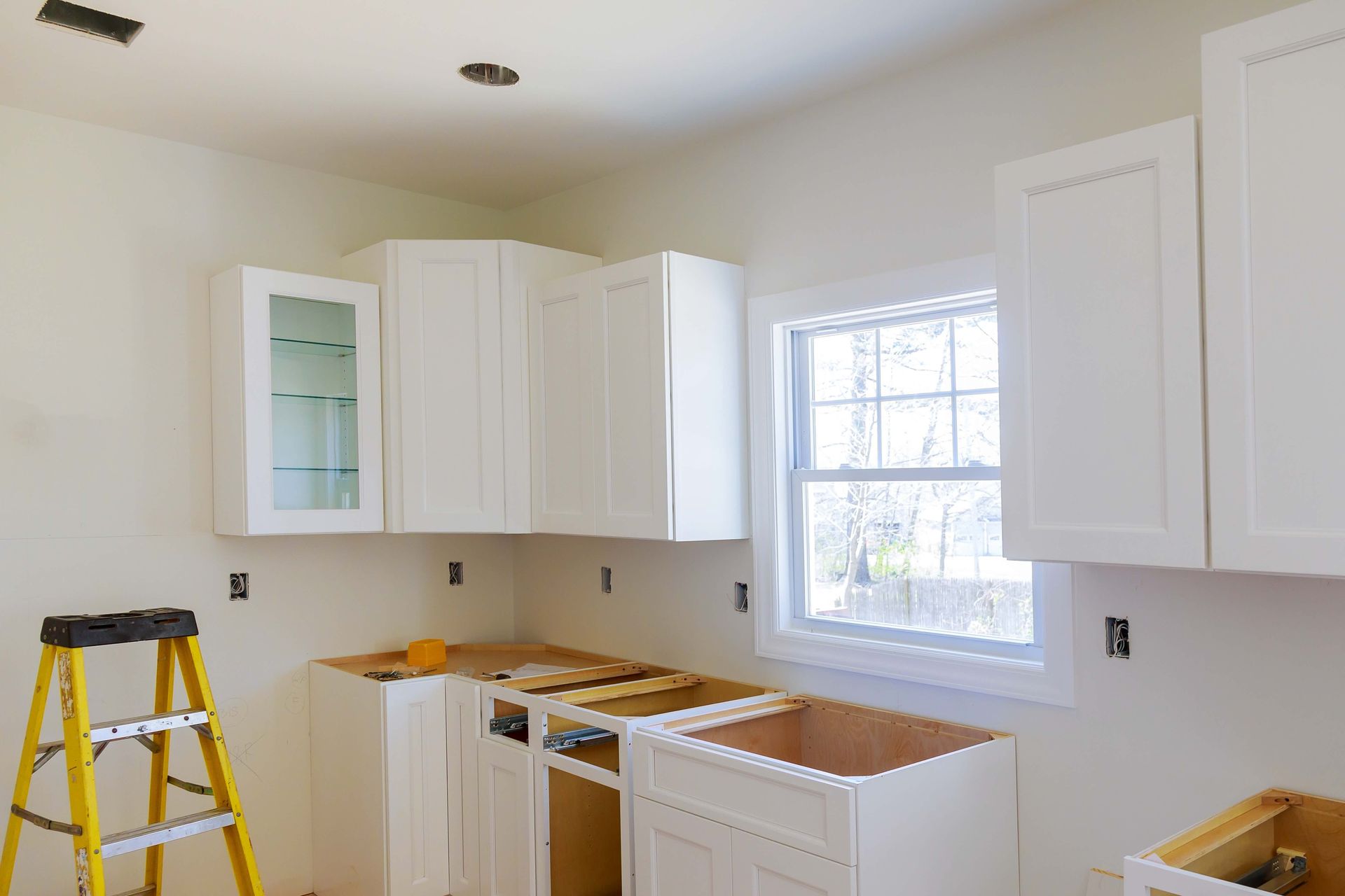 A kitchen under construction with white cabinets and a yellow ladder.