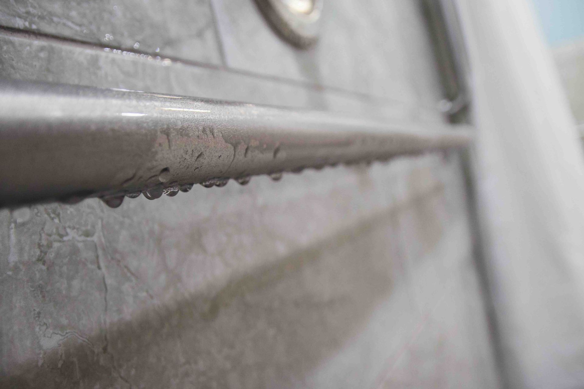 A close-up of a shower grab bar with water drops on it.