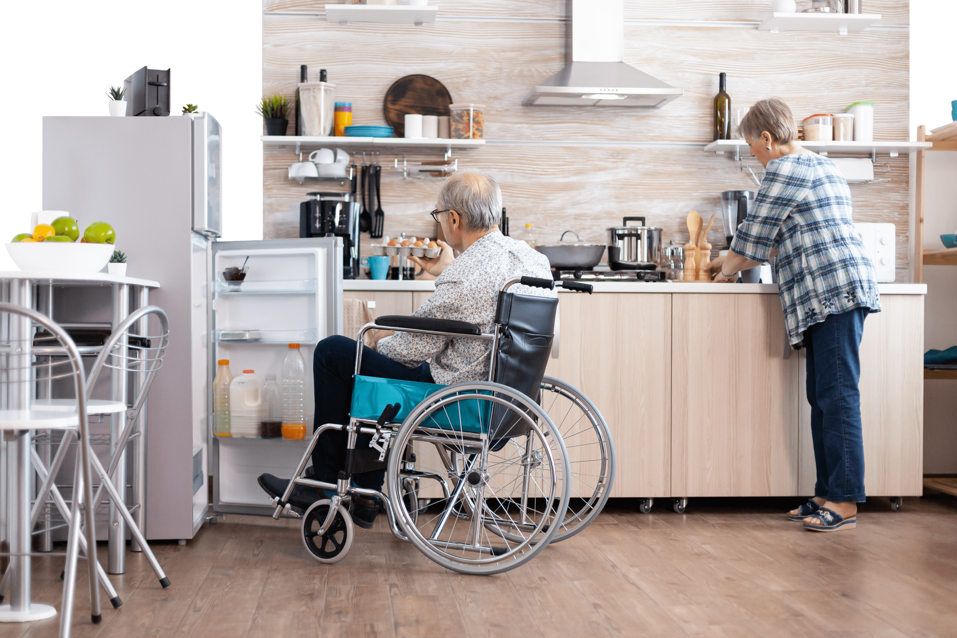 an elderly man in a wheelchair is looking into a refrigerator.