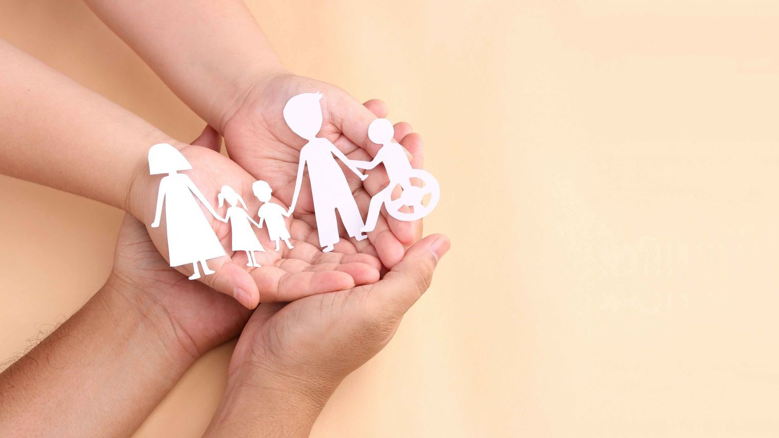 A paper cutout of a family with one person in a wheelchair is being held in a person's hands.