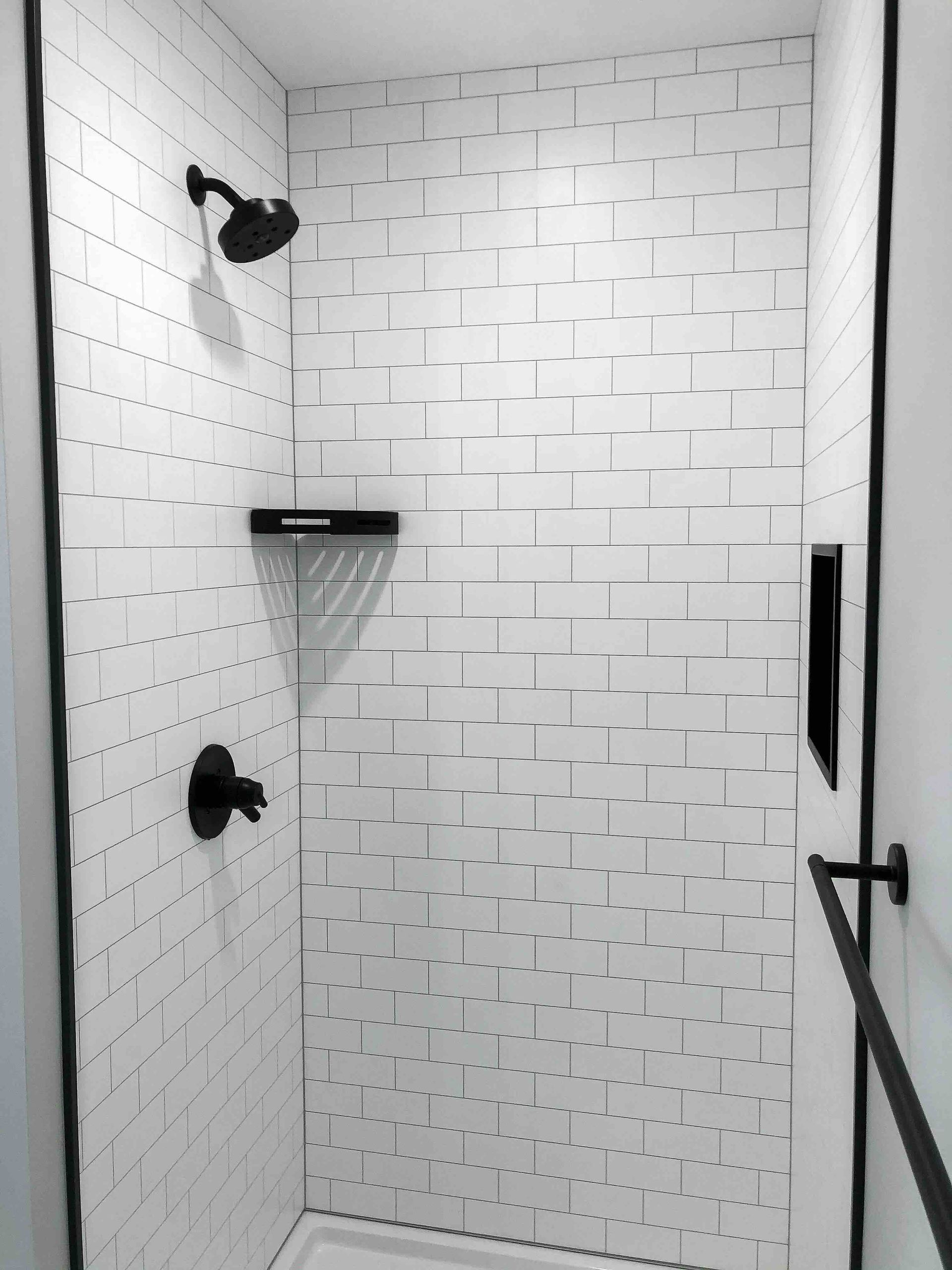 a shower with white tiles and a black shower head.
