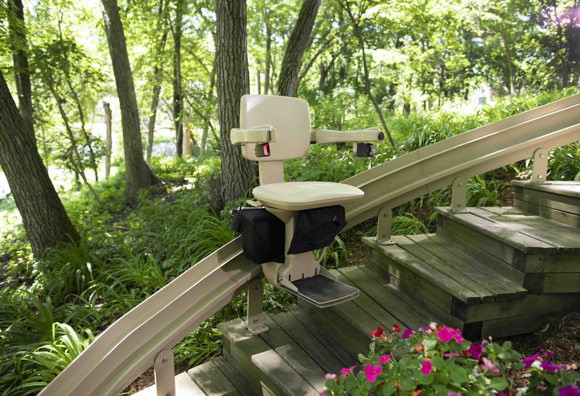 An outdoor stair lift mounted on a wooden staircase in a lush, green wooded setting.